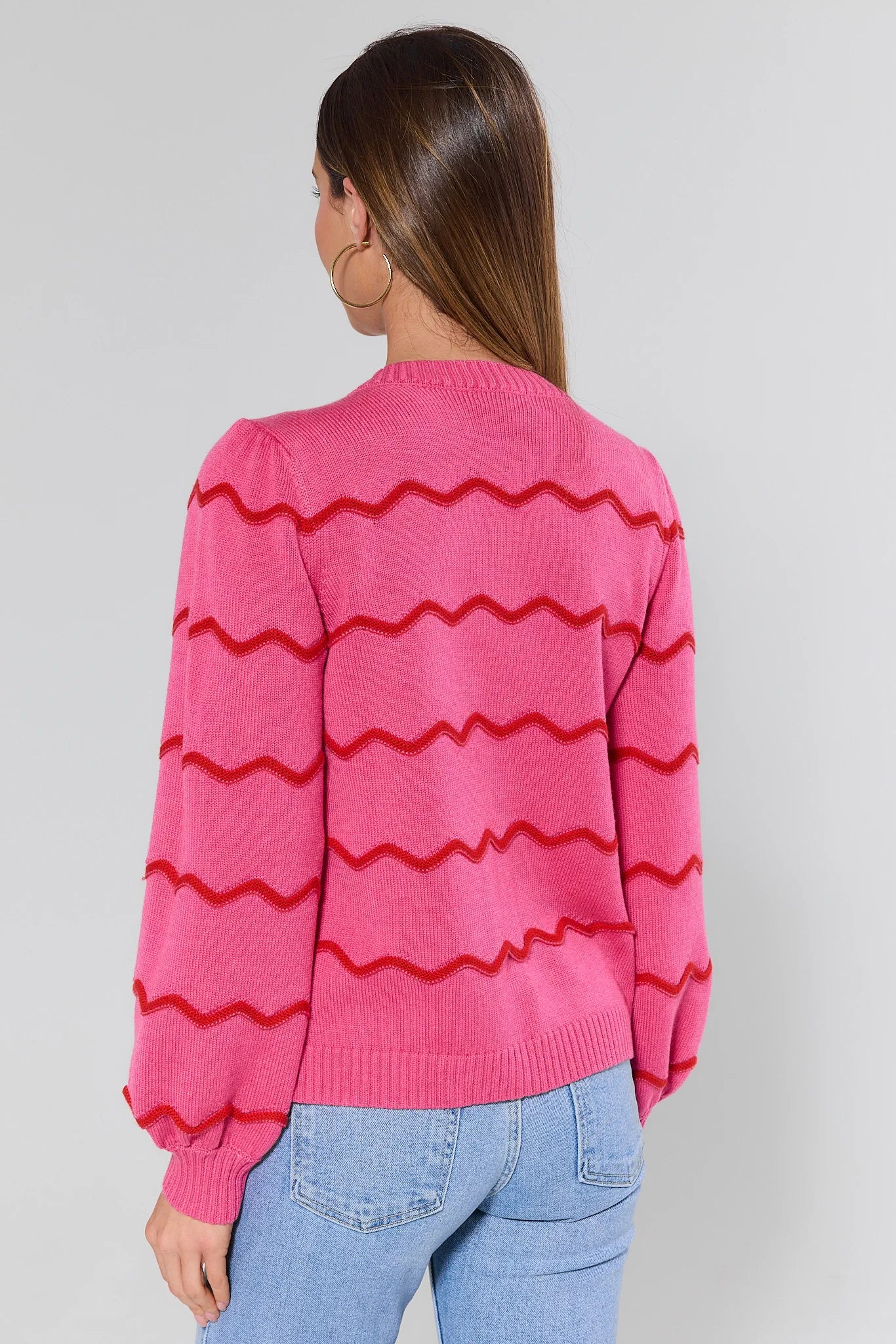 Person wearing a pink sweater with red zigzag patterns on a plain background
