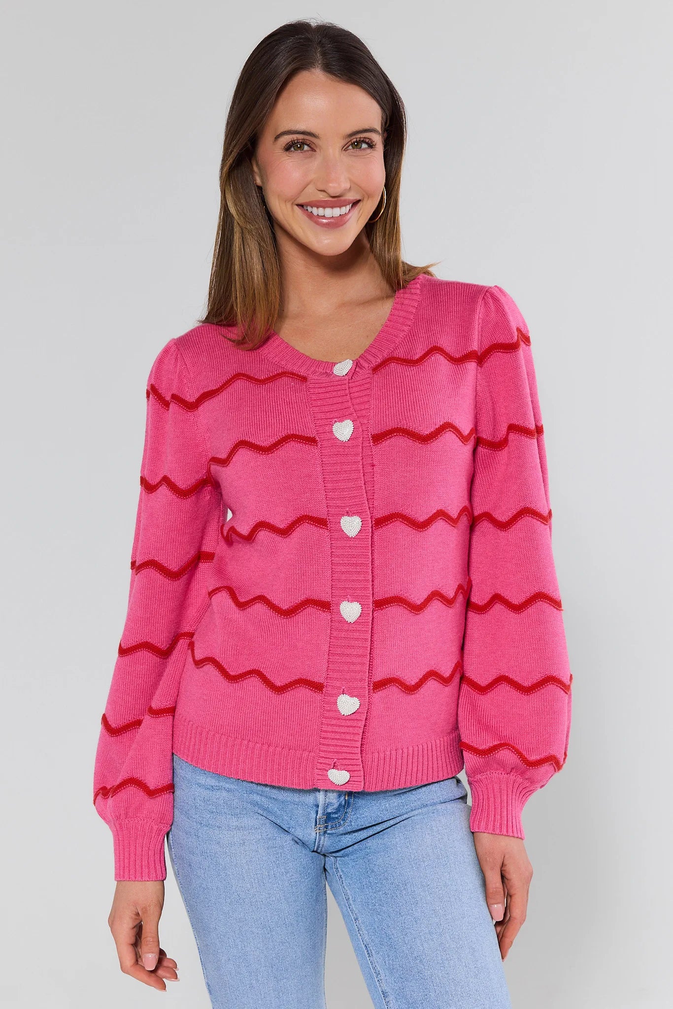 Woman wearing a pink cardigan with red wavy patterns on a plain background