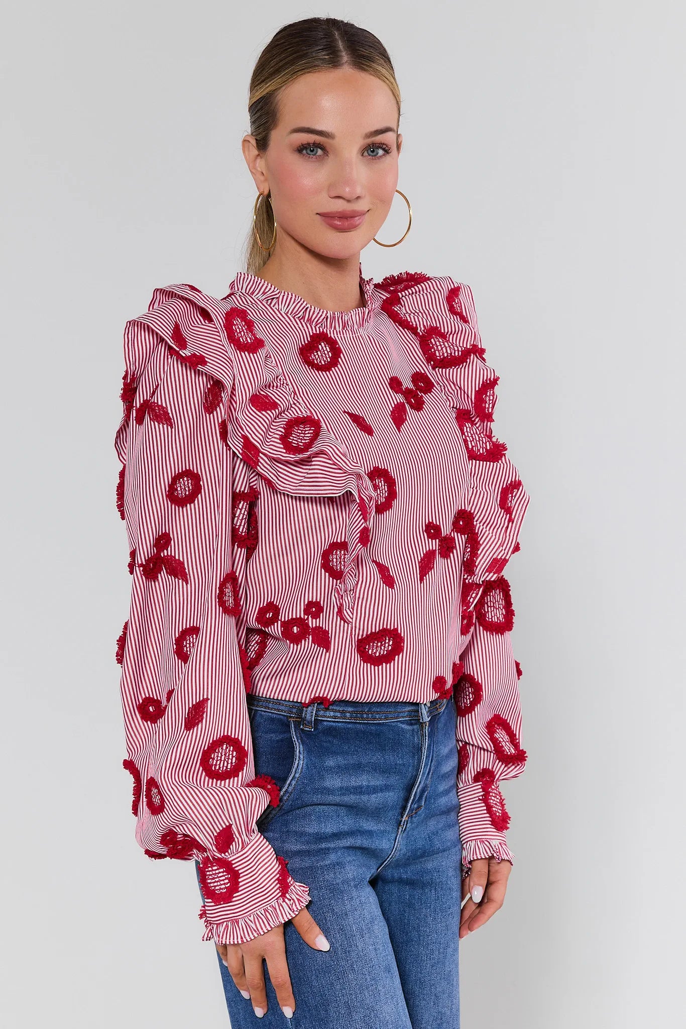 Woman wearing a pink blouse with red floral patterns and blue jeans on a white background