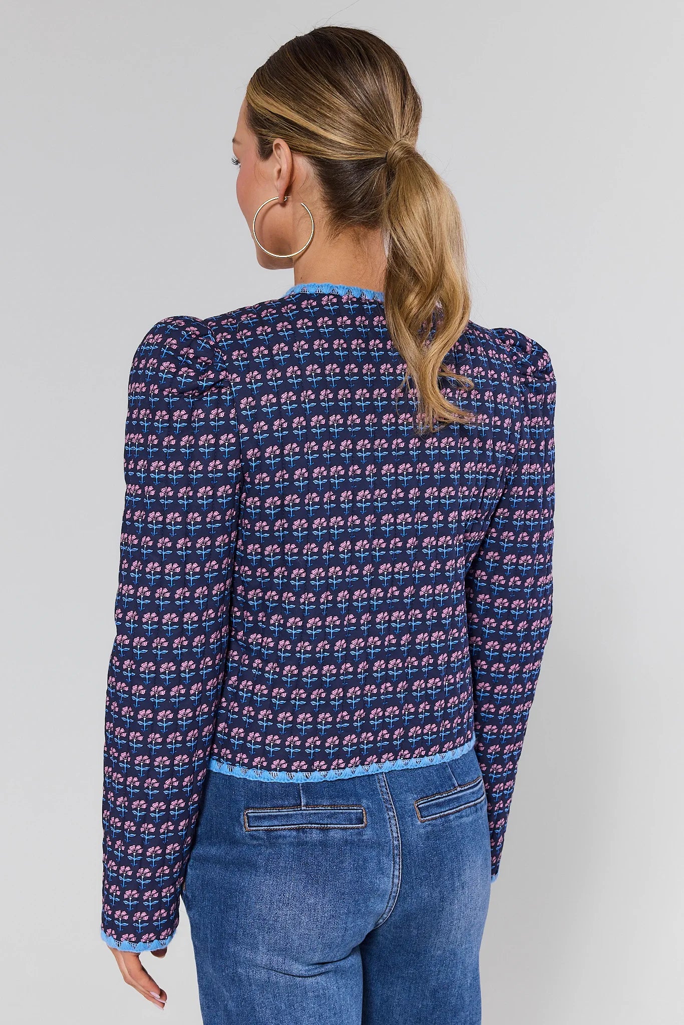 Woman wearing a blue patterned long-sleeve shirt and jeans on a plain background