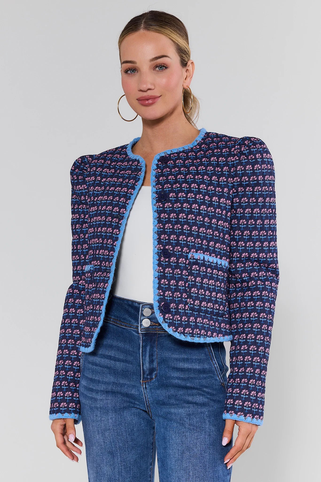 Woman wearing a patterned blue jacket and jeans on a plain background