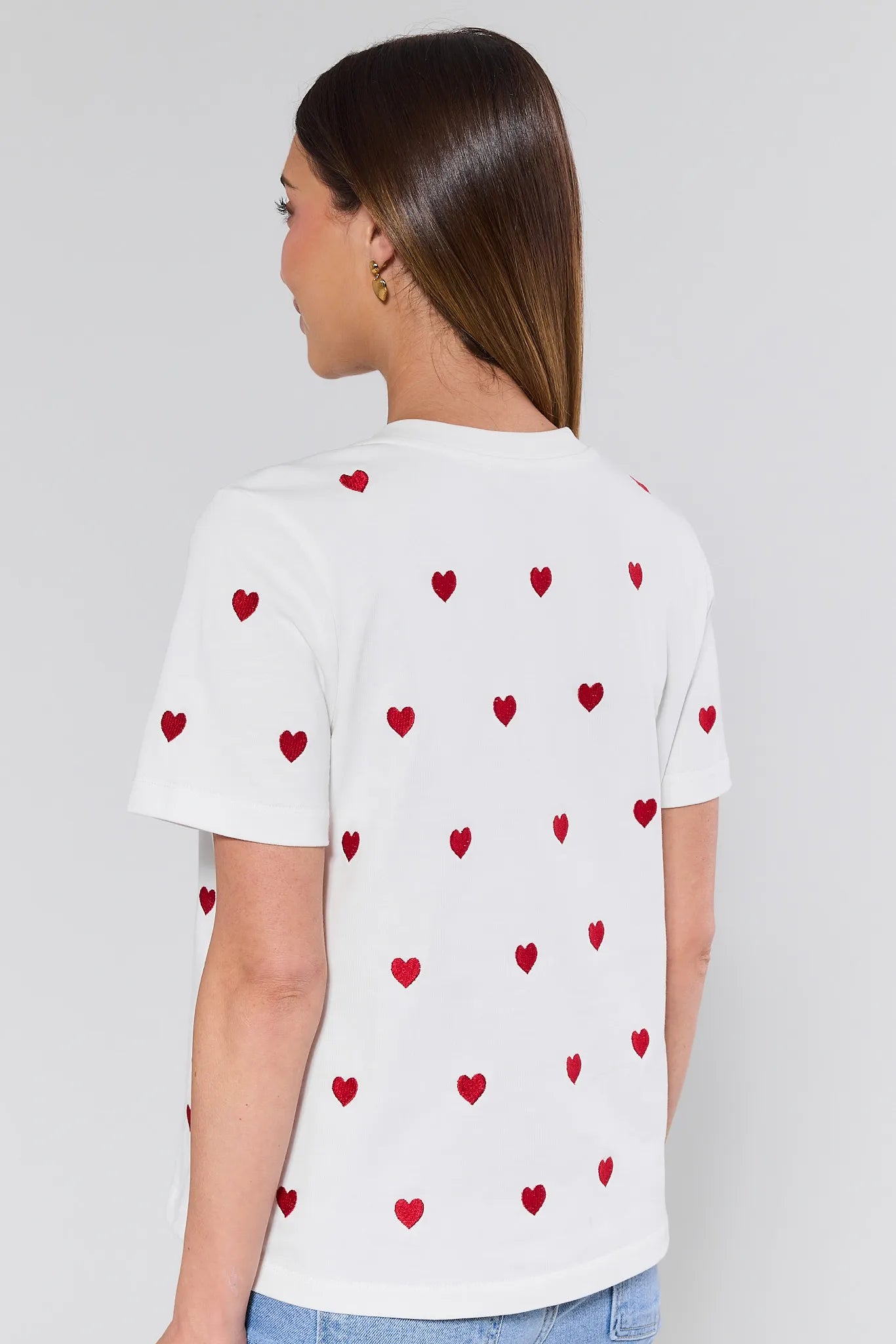 White t-shirt with red heart patterns worn by a person on a plain background
