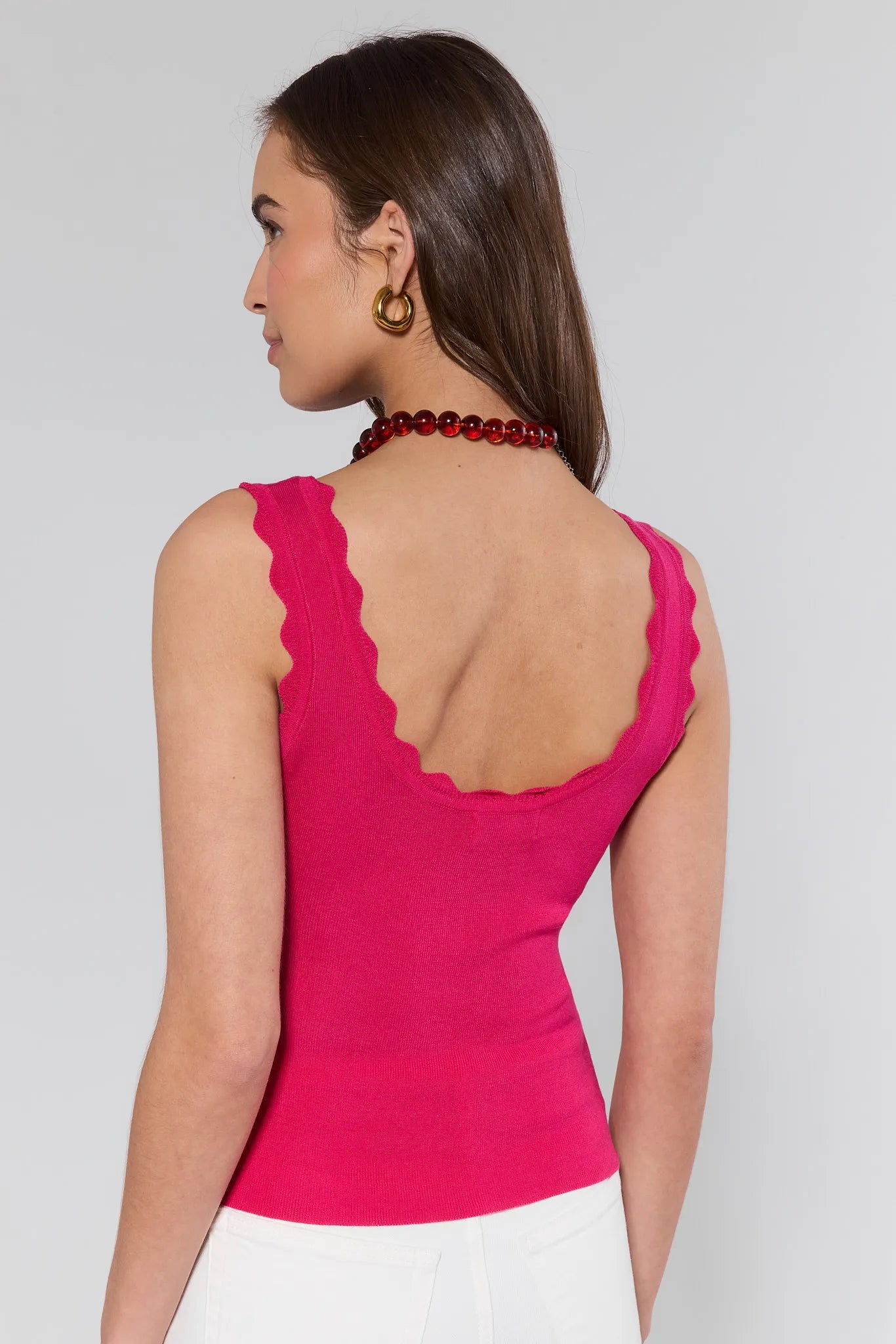 Woman wearing a pink sleeveless top with a scalloped neckline on a plain background