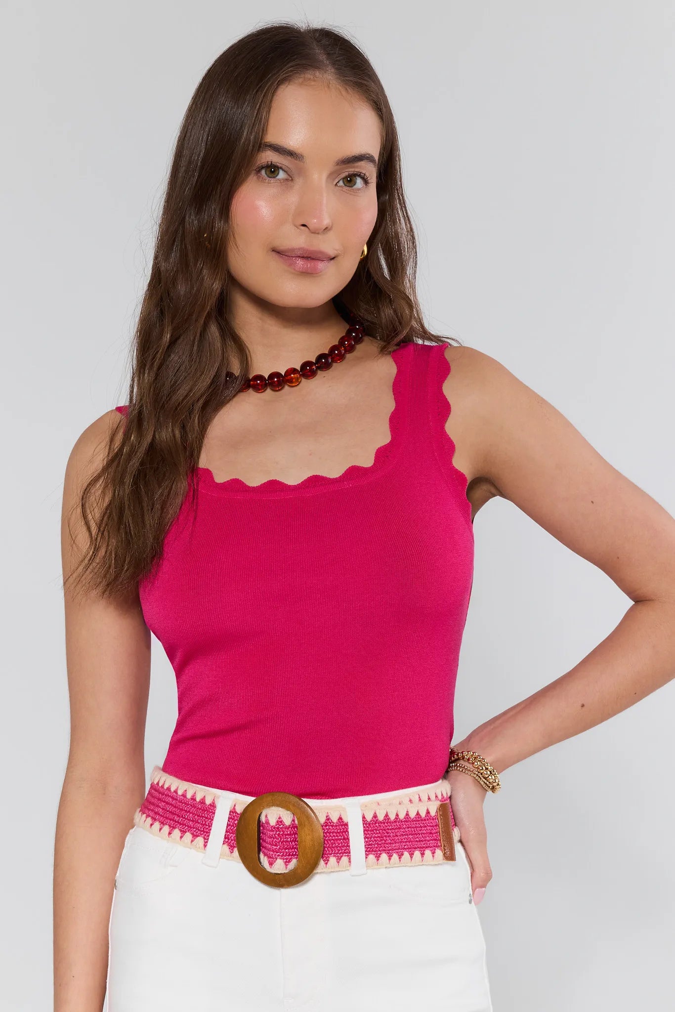 Woman wearing a bright pink top and white pants with a decorative belt against a plain background