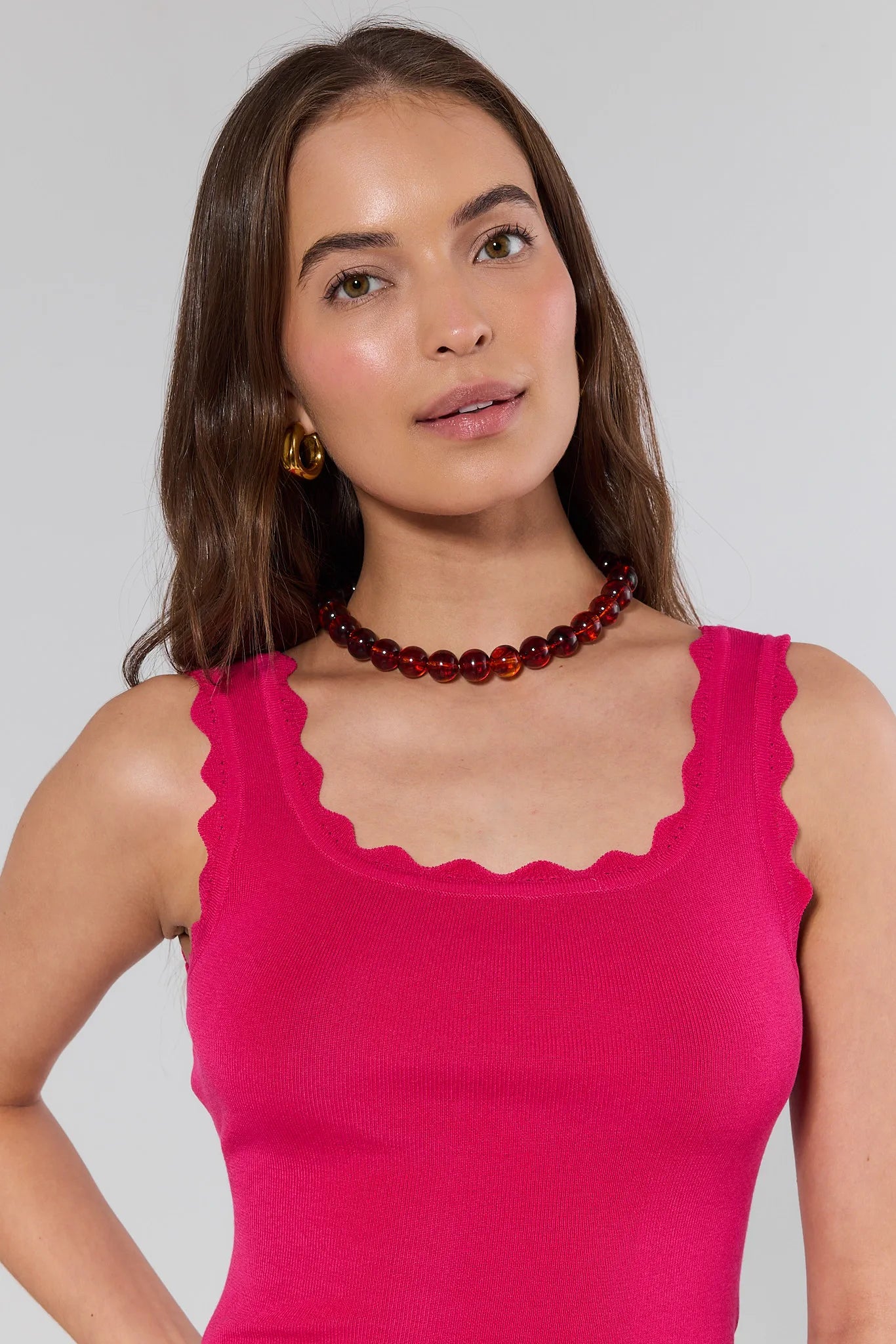 Woman wearing a bright pink sleeveless top with a scalloped neckline against a plain background.
