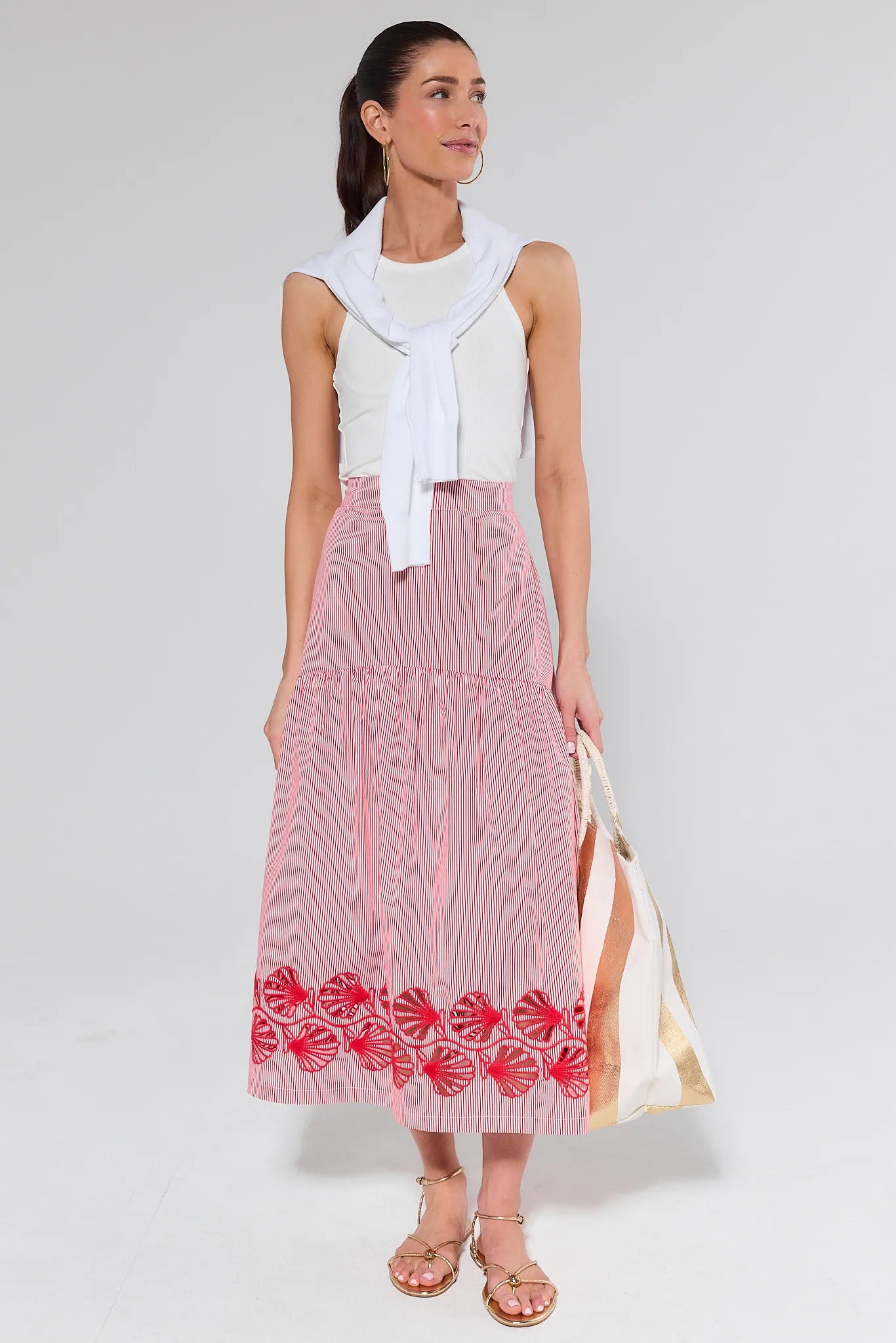 Woman wearing a white sleeveless top and red patterned skirt on a plain background