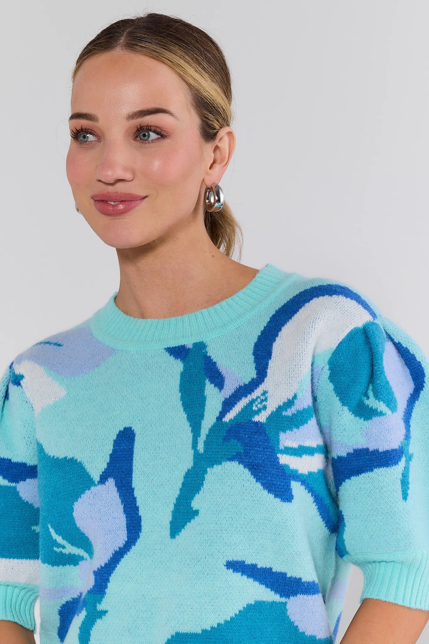 Woman wearing a light blue sweater with floral pattern against a white background