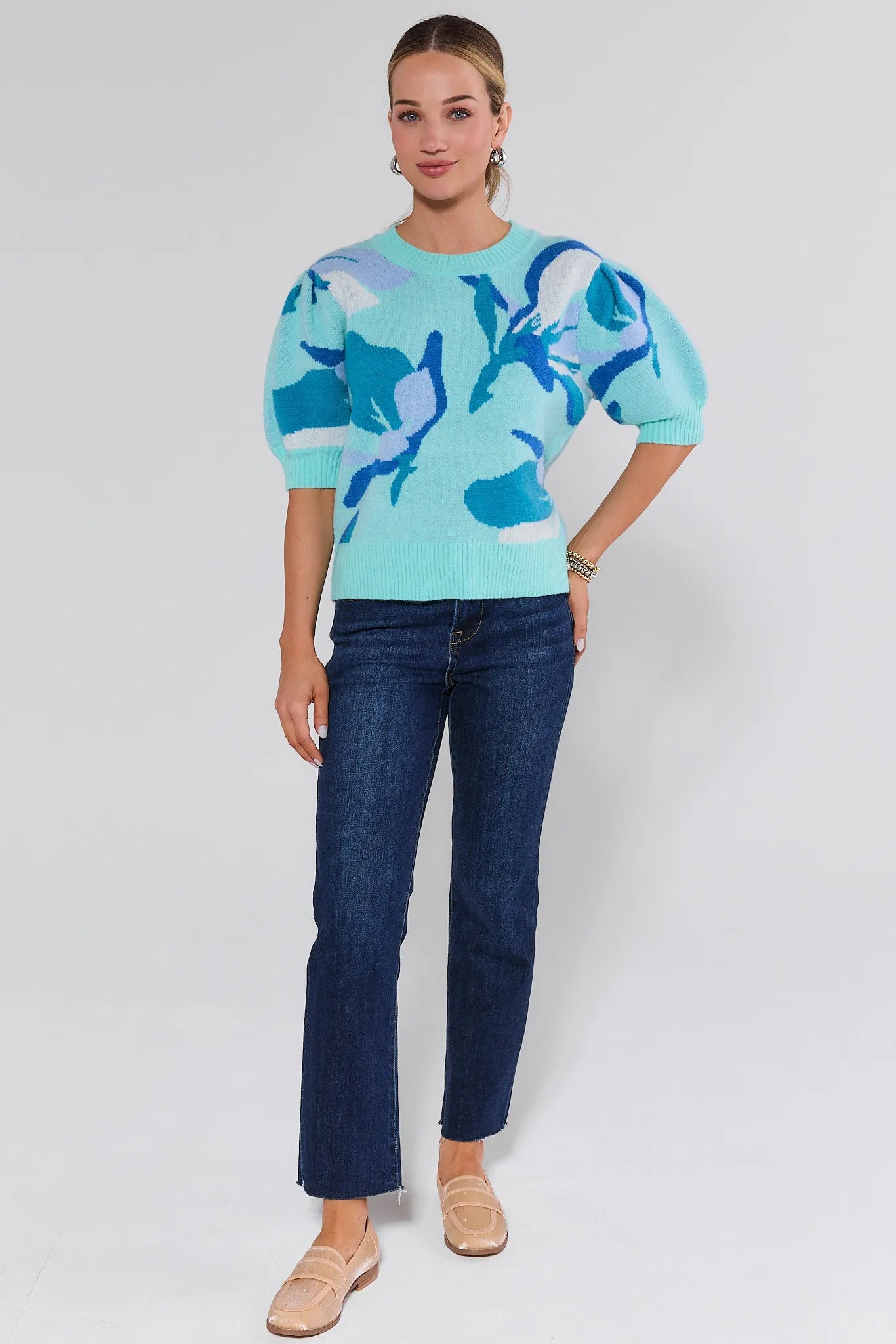 Woman wearing a light blue sweater with blue floral patterns and dark blue jeans on a white background