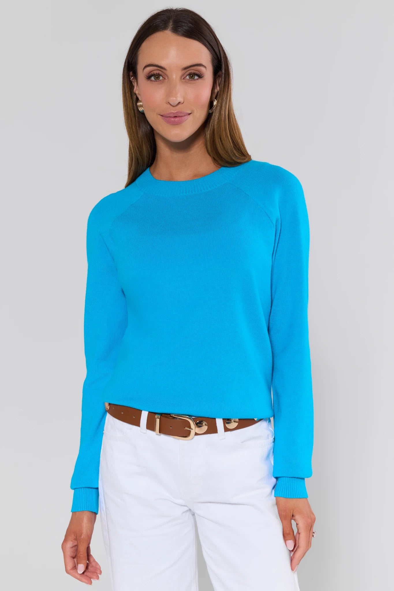Woman wearing a bright blue long-sleeve top and white pants against a plain background