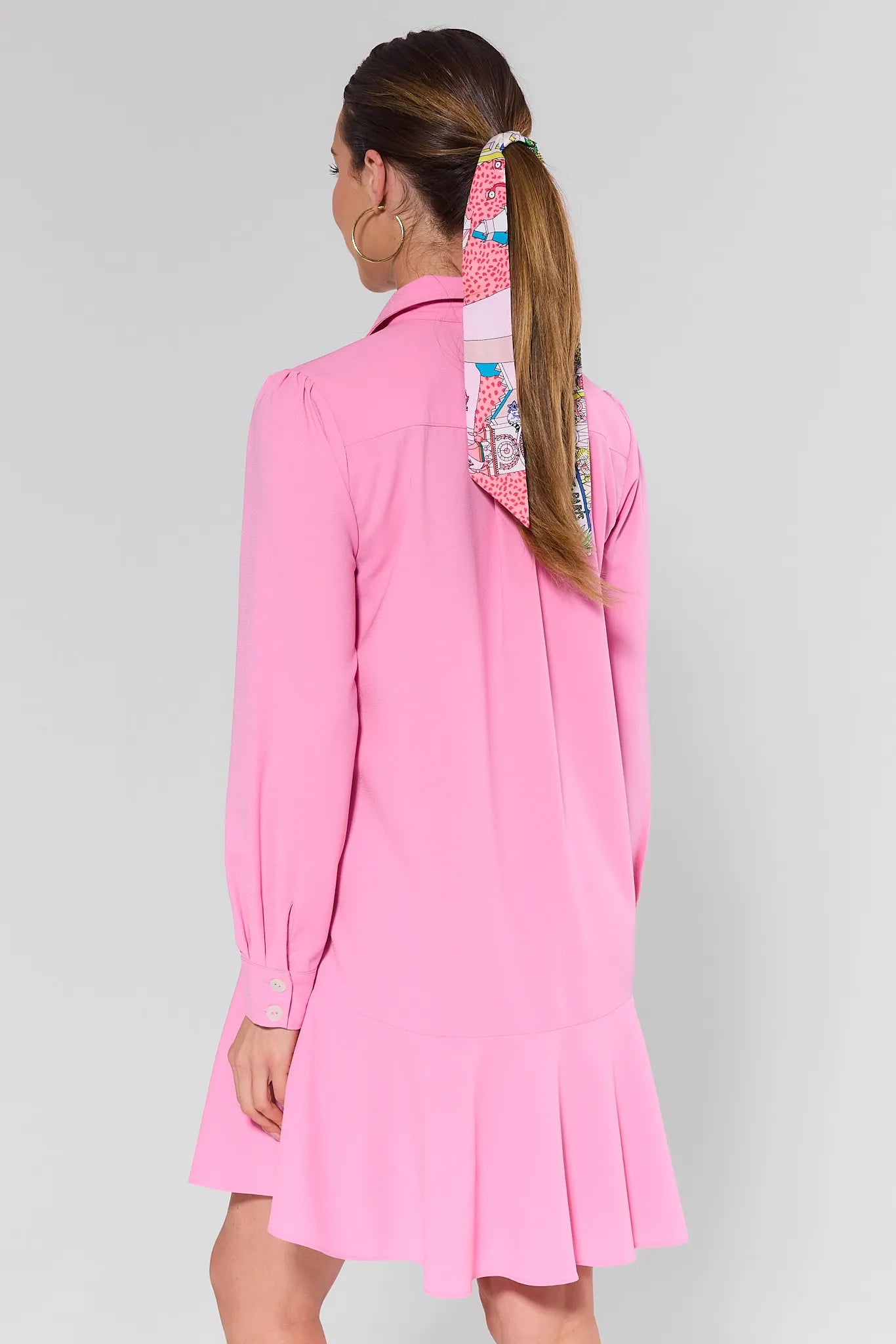 Person wearing a pink dress with a colorful headscarf on a gray background