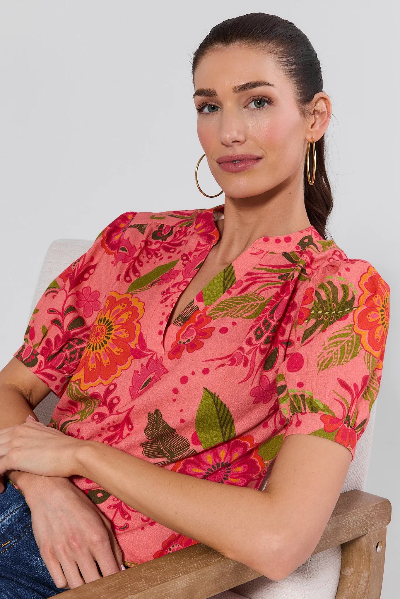 Woman wearing a pink floral blouse sitting on a chair against a white background