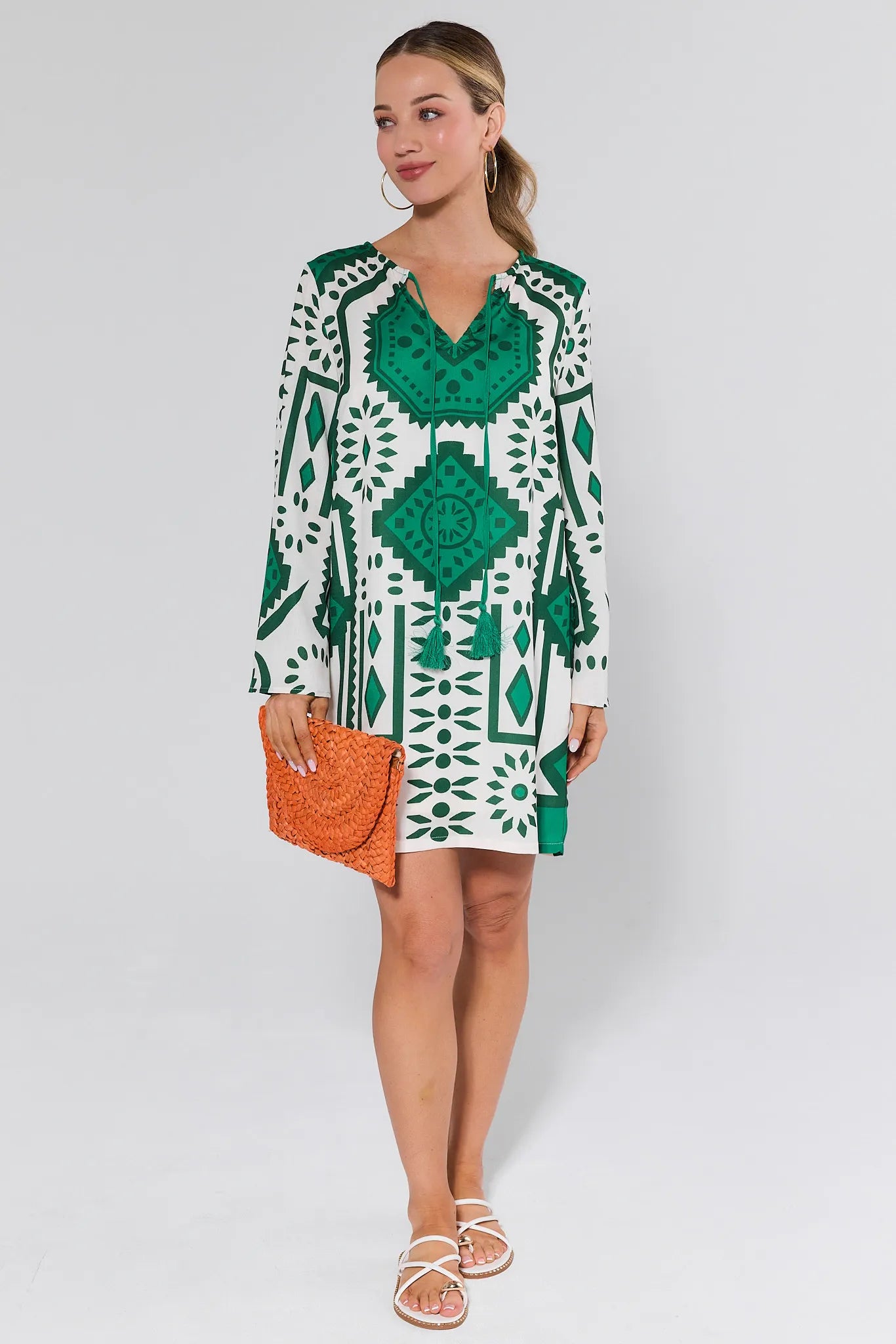 Woman wearing a green and white patterned dress with an orange clutch against a white background