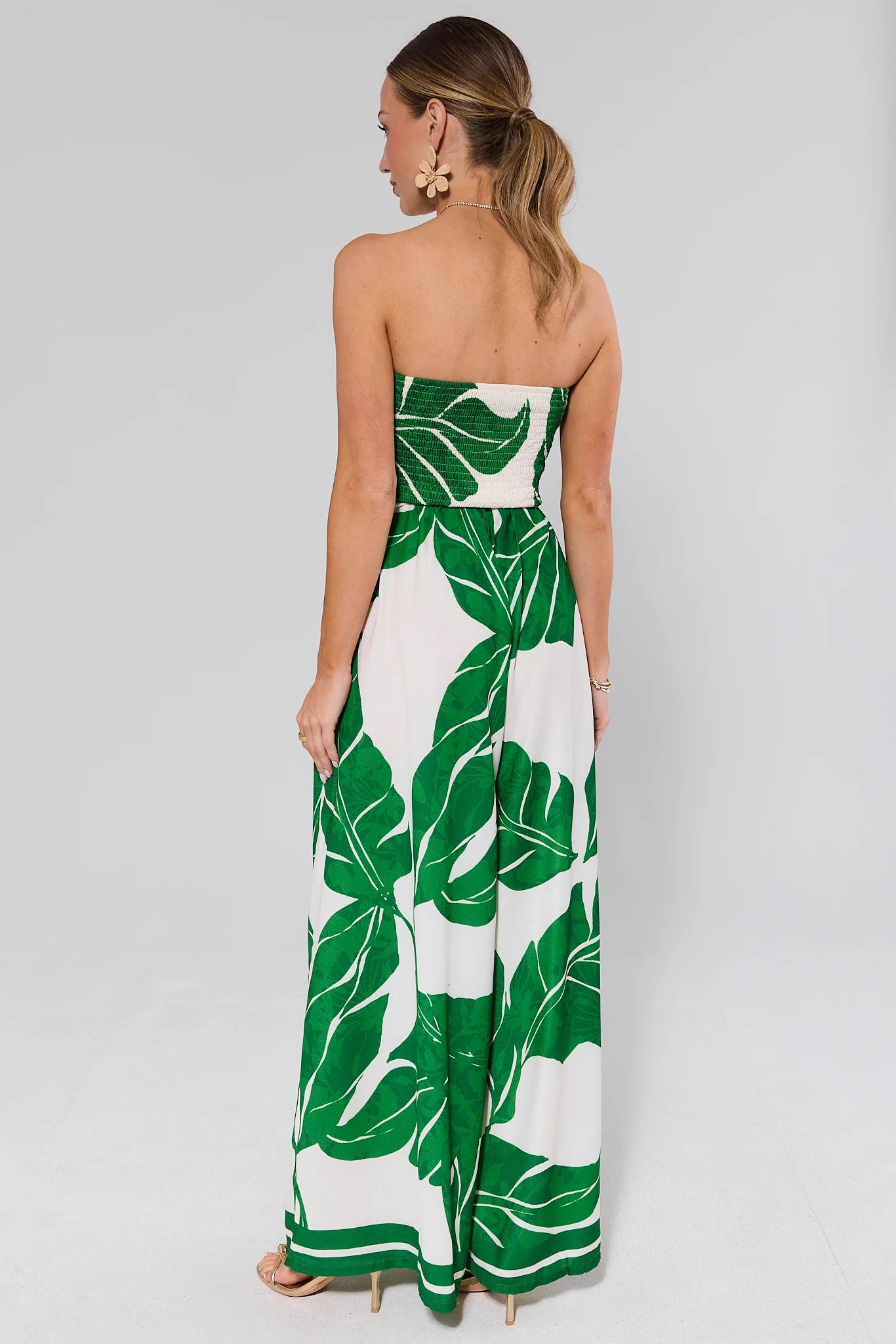 Woman standing wearing a strapless dress with green leaf pattern on a white background