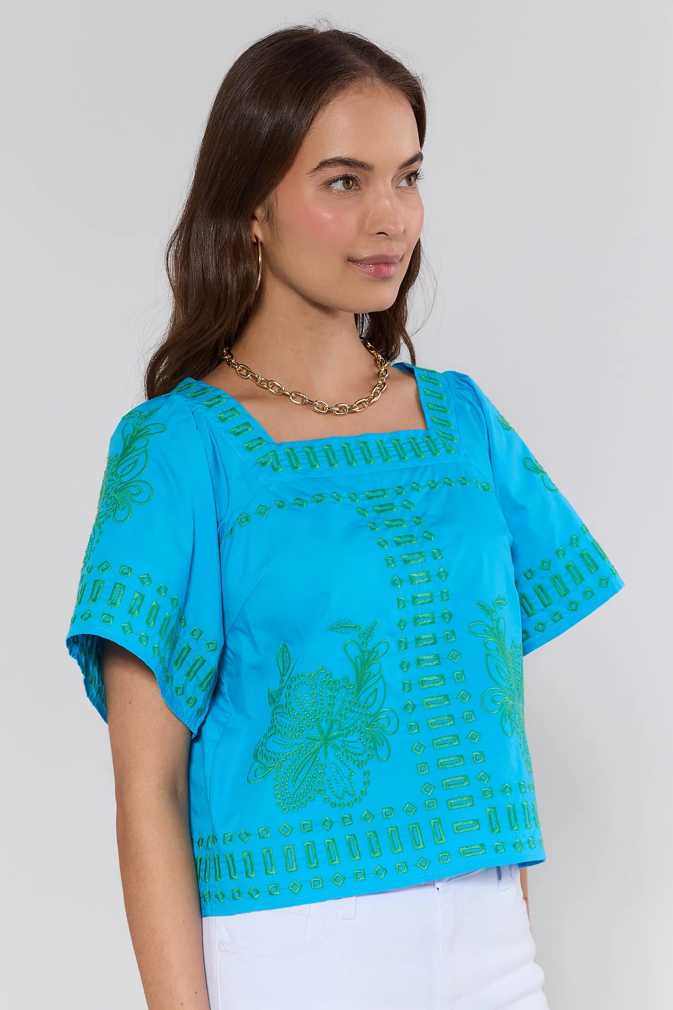 Woman wearing a blue top with green patterns on a plain background