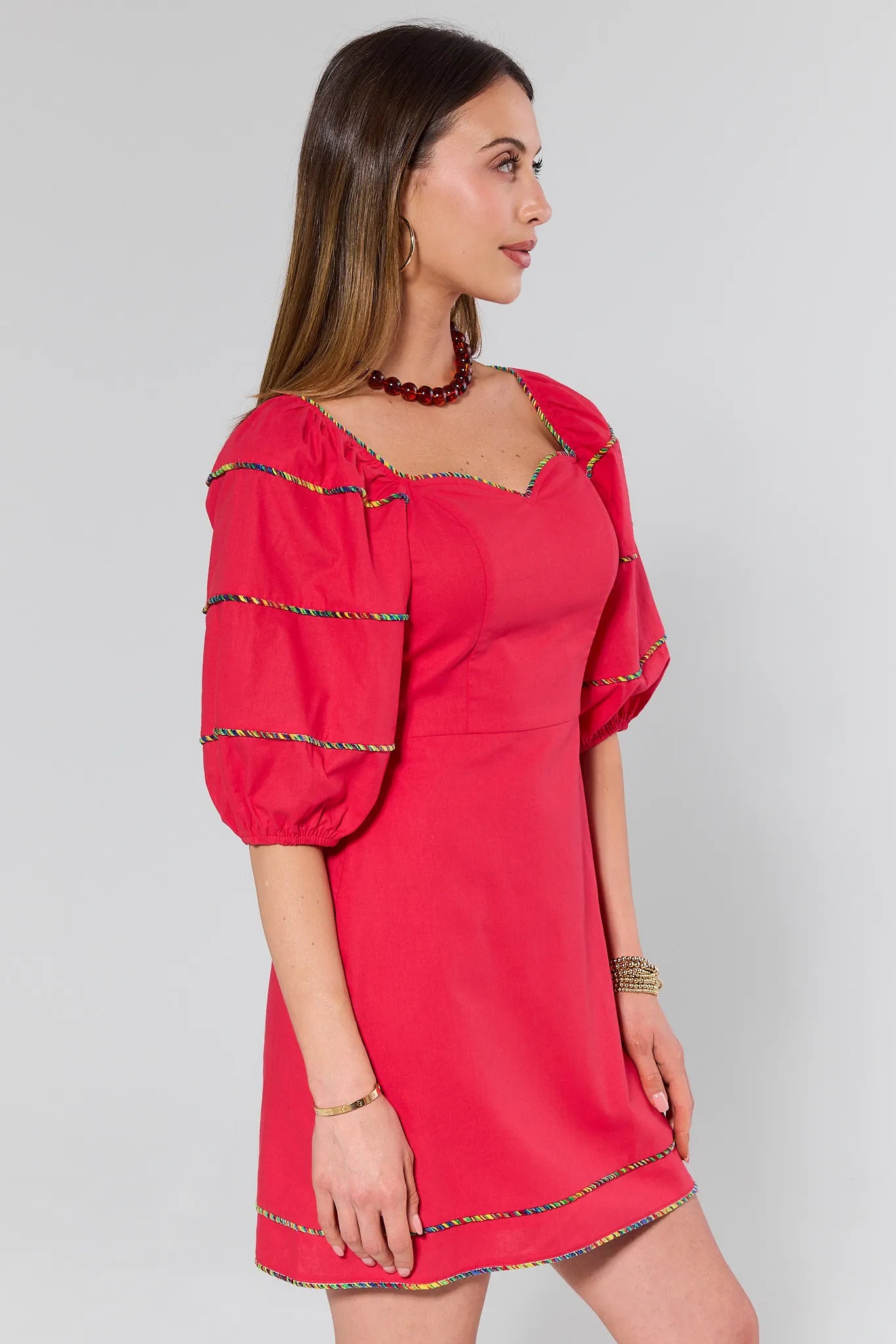 Woman wearing a red dress with colorful trim on a gray background