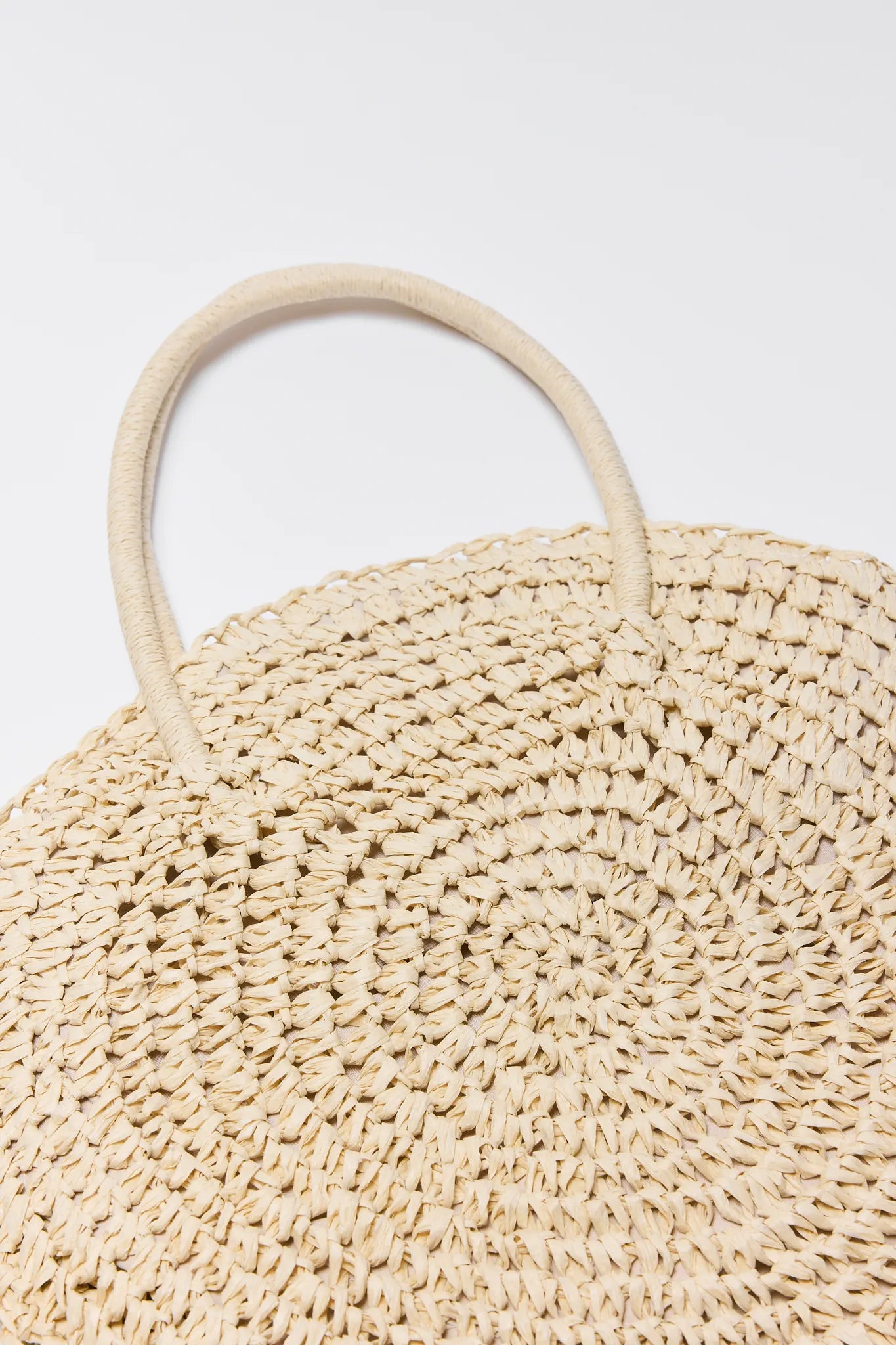 Close-up of a Josie Raffia Woven Bucket Bag with circular handles on a light gray background