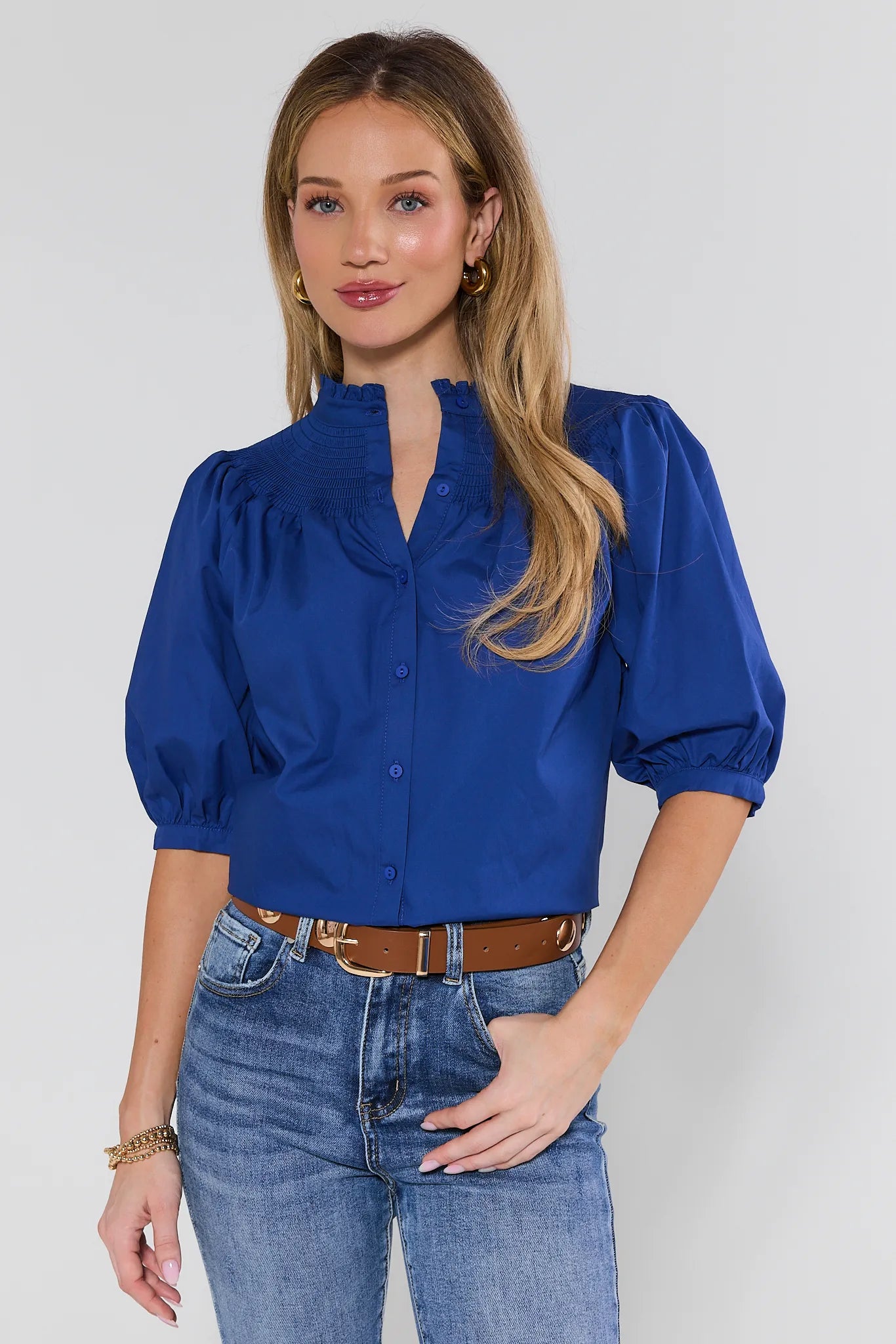 Woman wearing a blue blouse and jeans against a plain background