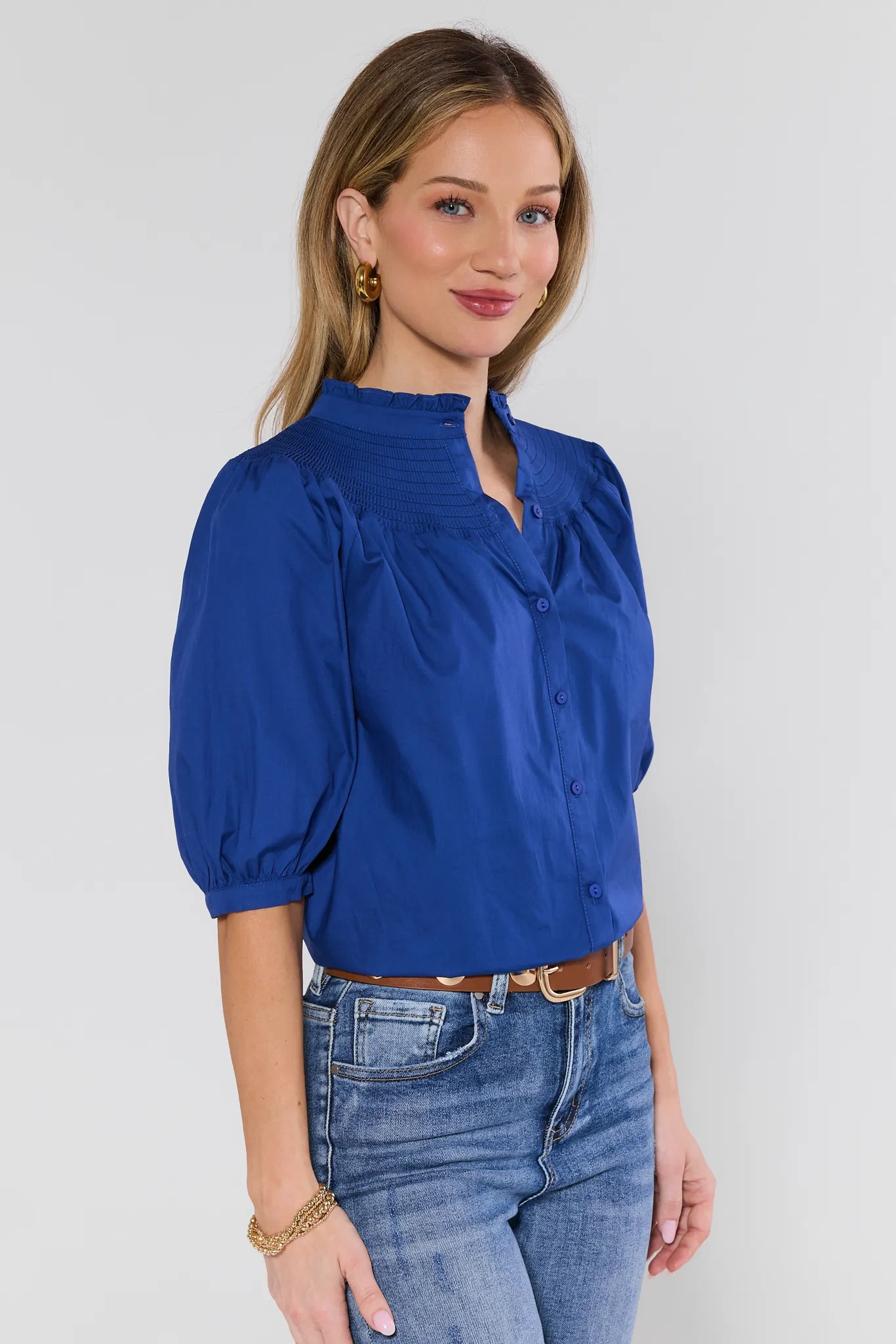 Woman wearing a blue blouse and jeans against a plain background