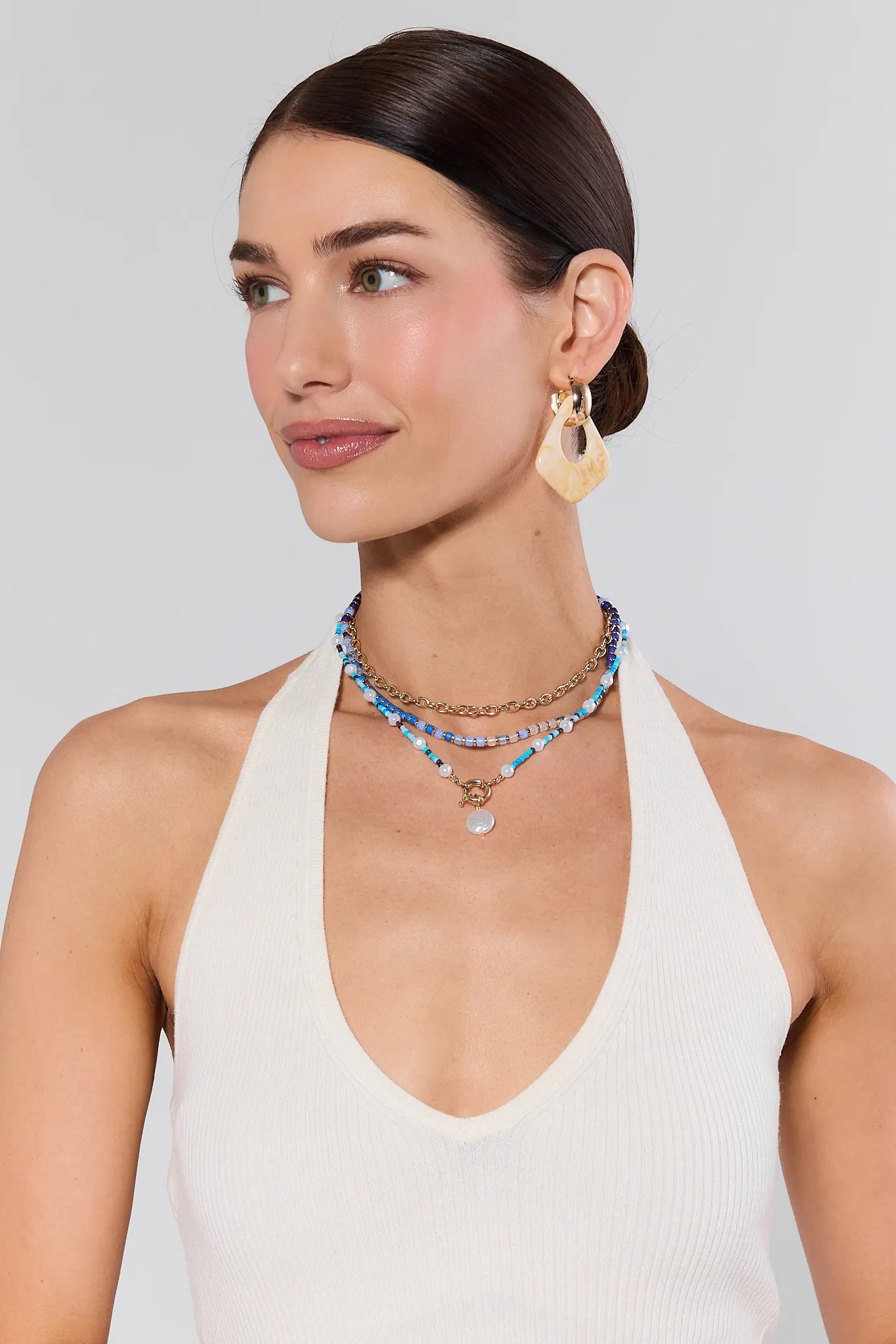 Woman wearing layered necklaces and earrings on a plain background