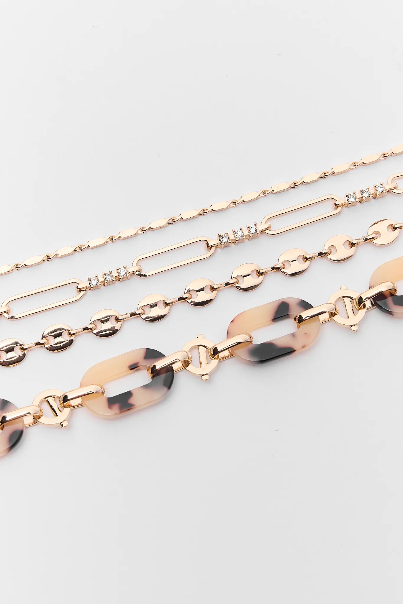Three gold chain necklaces with tortoiseshell accents on a light gray background