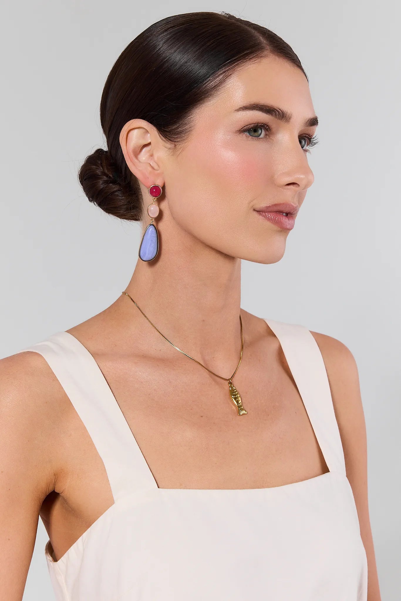 Woman wearing colorful earrings and a necklace against a plain background
