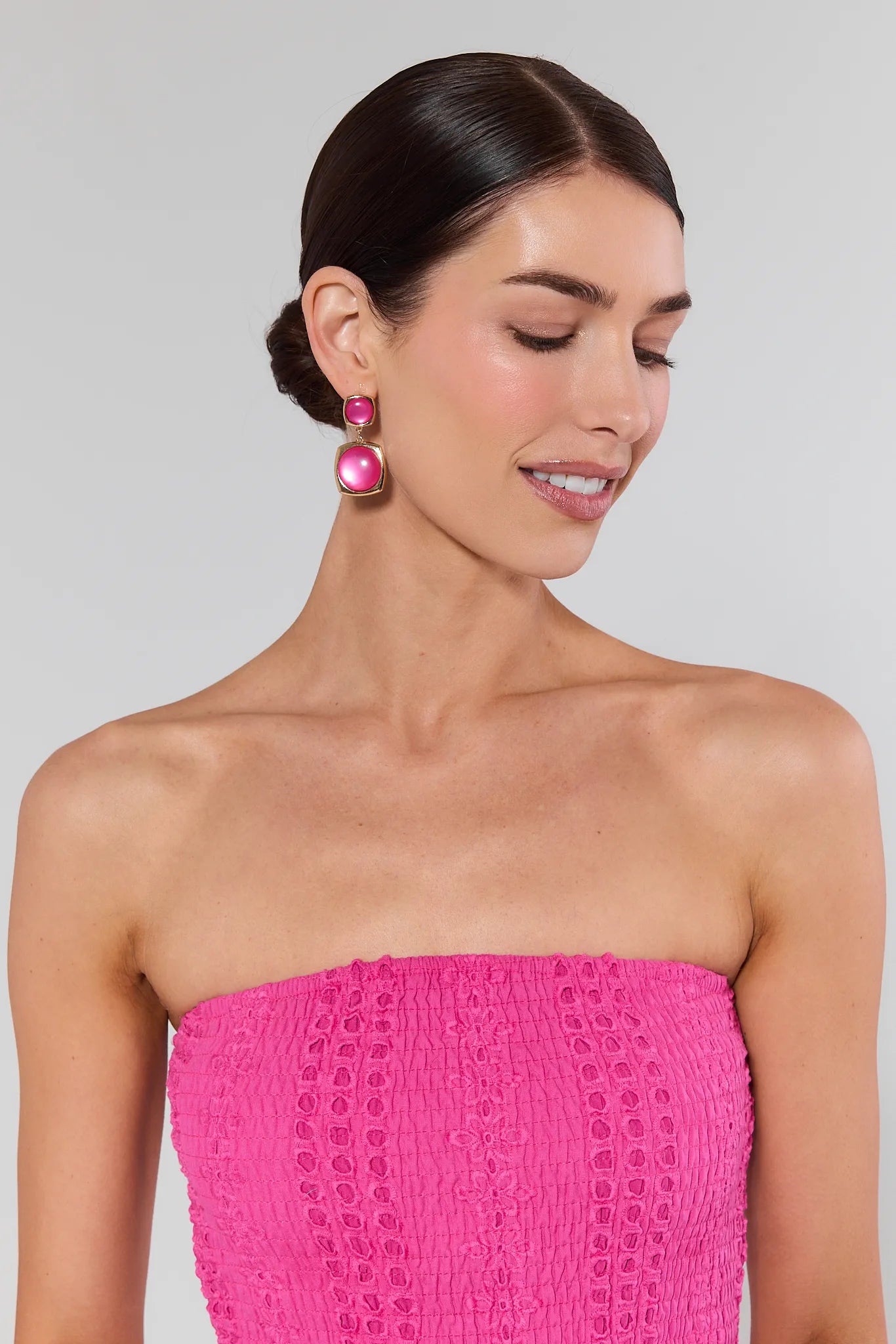 Woman wearing a pink strapless dress and earrings against a gray background