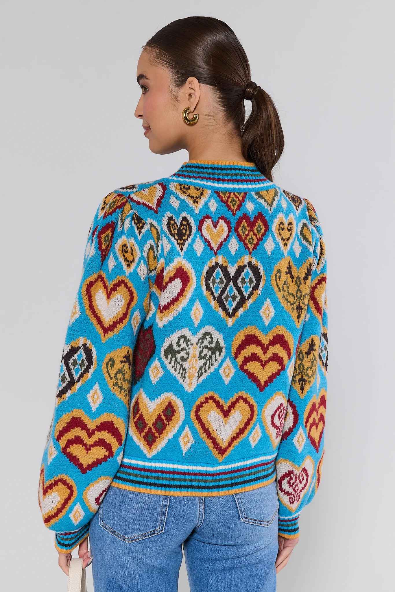 Person wearing a colorful heart-patterned Cammie Blue Heart Knit Sweater against a plain background