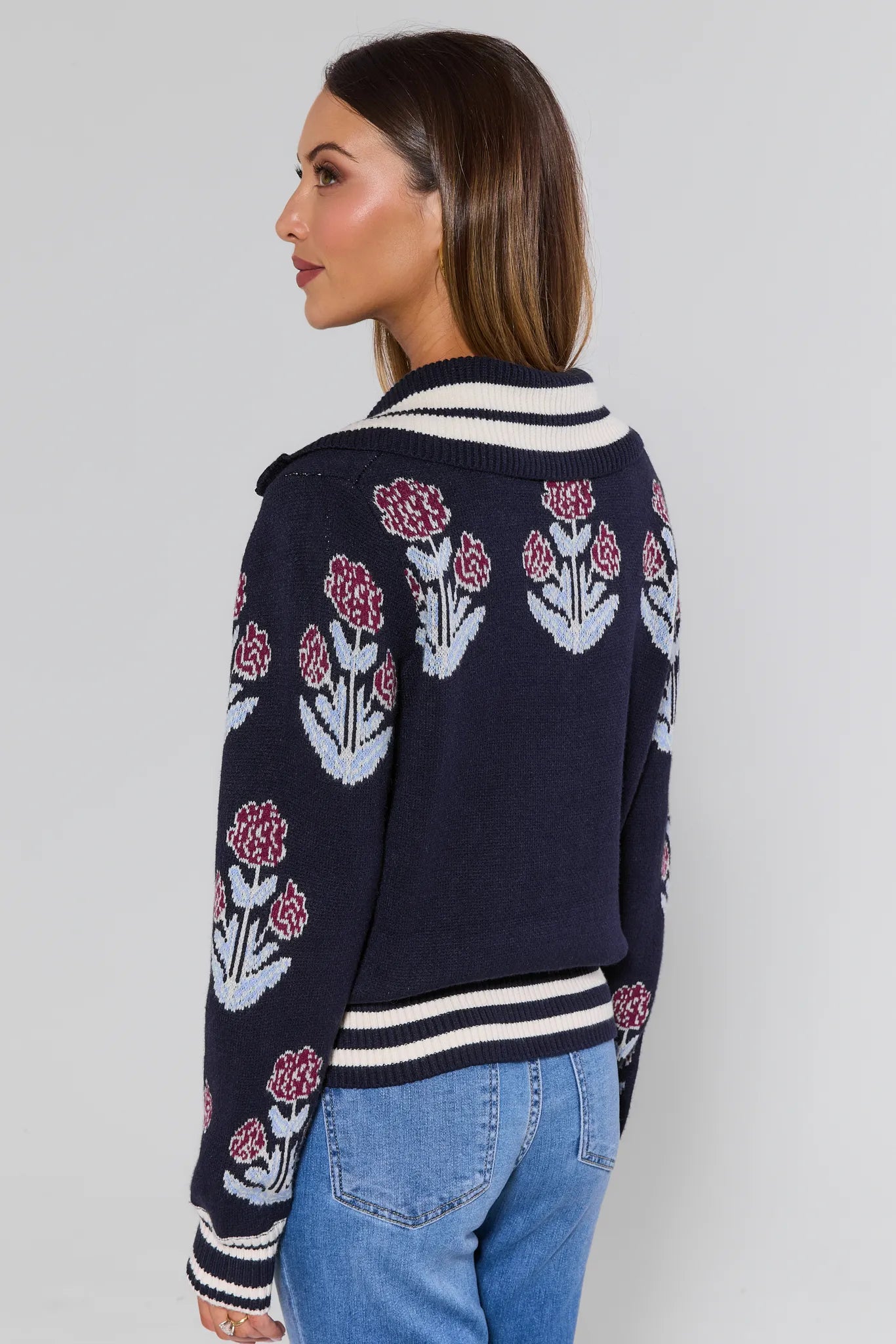Woman wearing a Corrine Floral Zip Up Cardigan navy blue with floral patterns back of sweater on a plain background