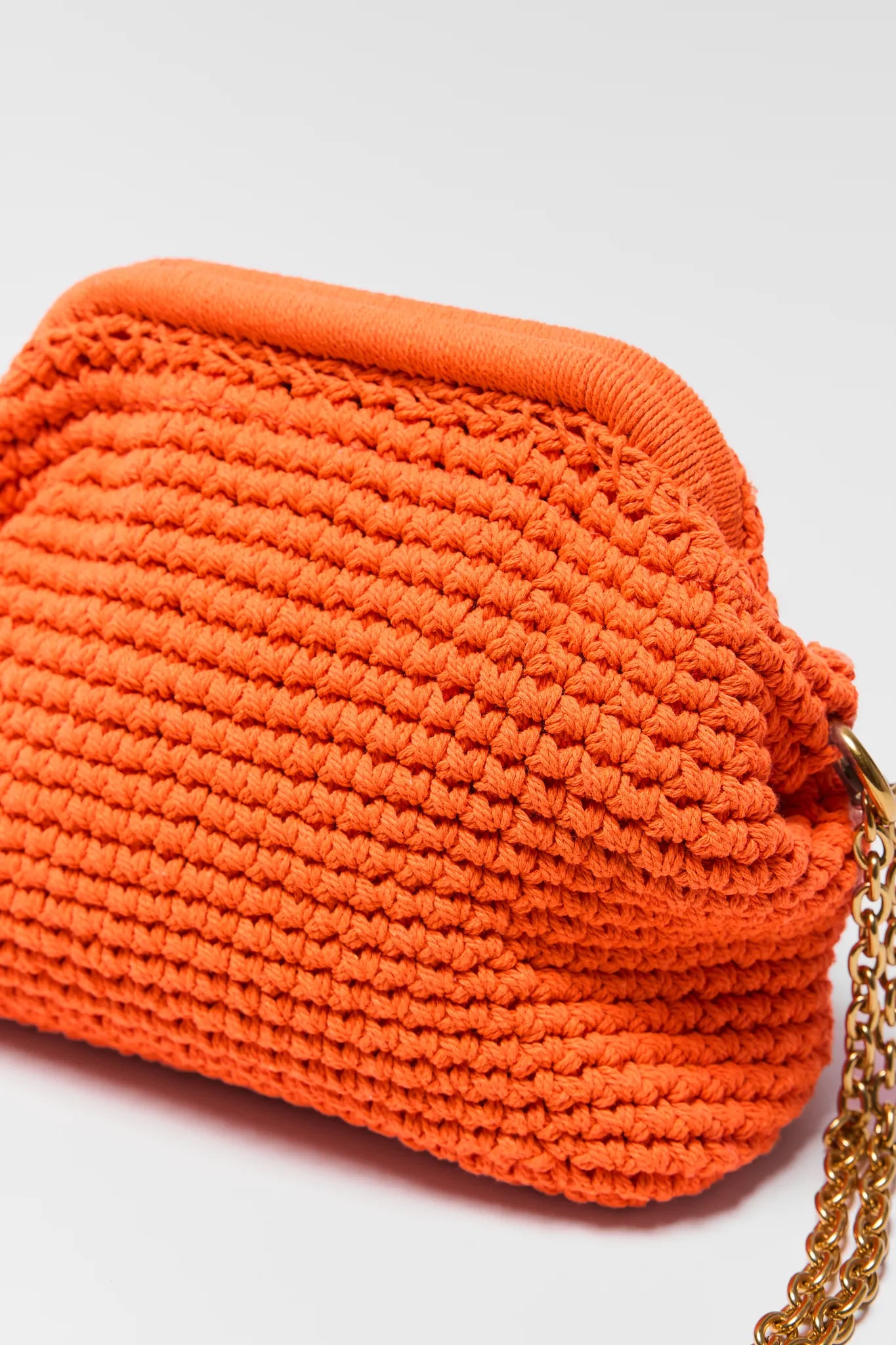 Close up of Gabbie Orange Crochet Shoulder Bag with a gold chain on a light gray background