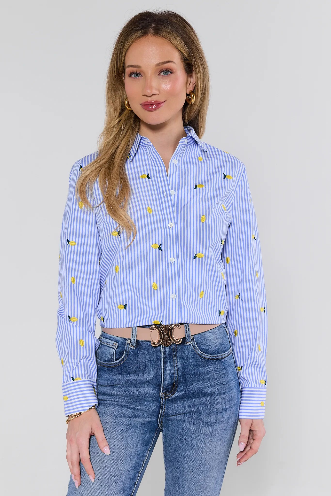Woman wearing a blue striped shirt with yellow pattern and jeans on a plain background