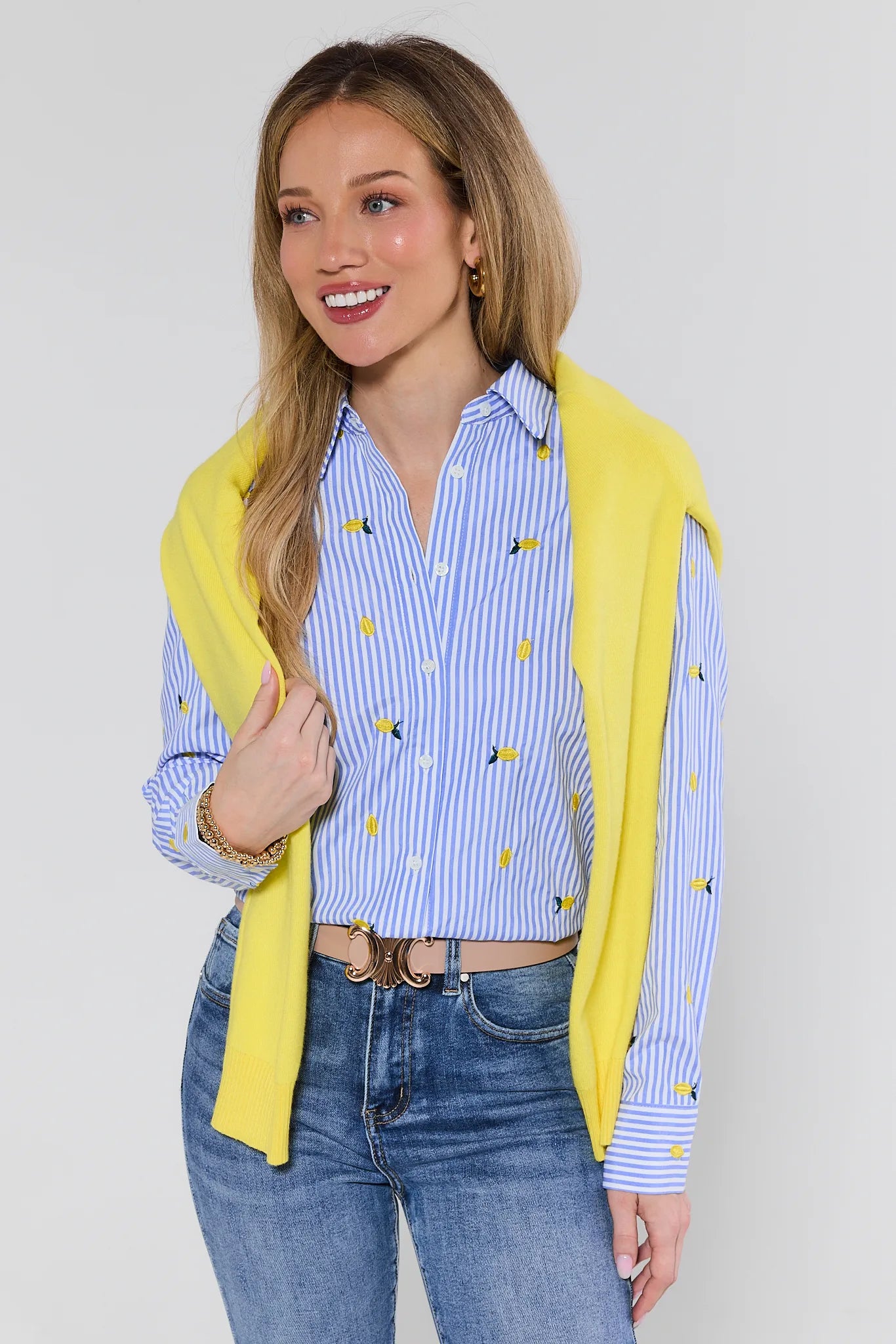 Woman wearing a yellow cardigan over a blue and white striped shirt with a white background