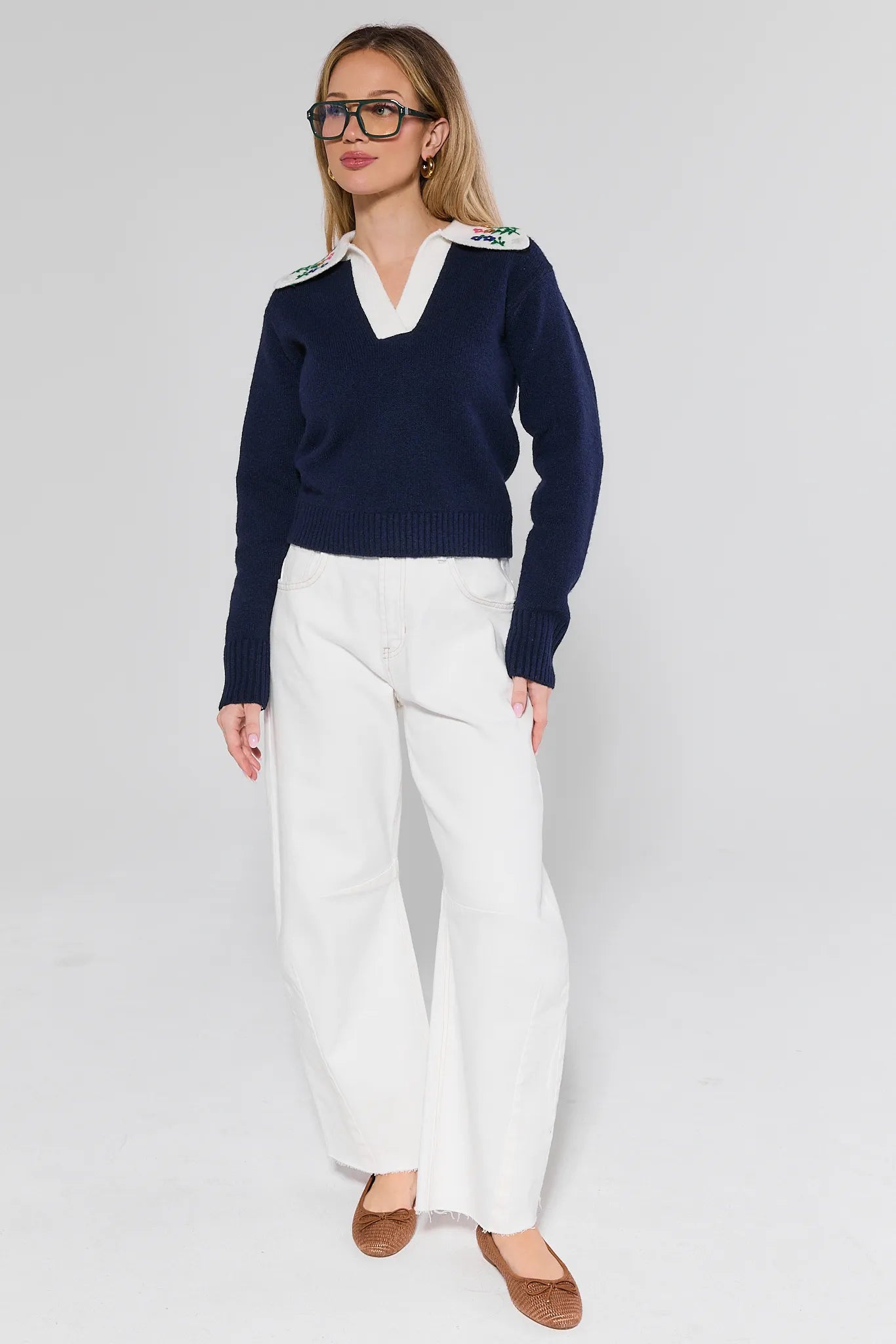 Woman wearing a navy sweater with white trim and white pants on a plain background