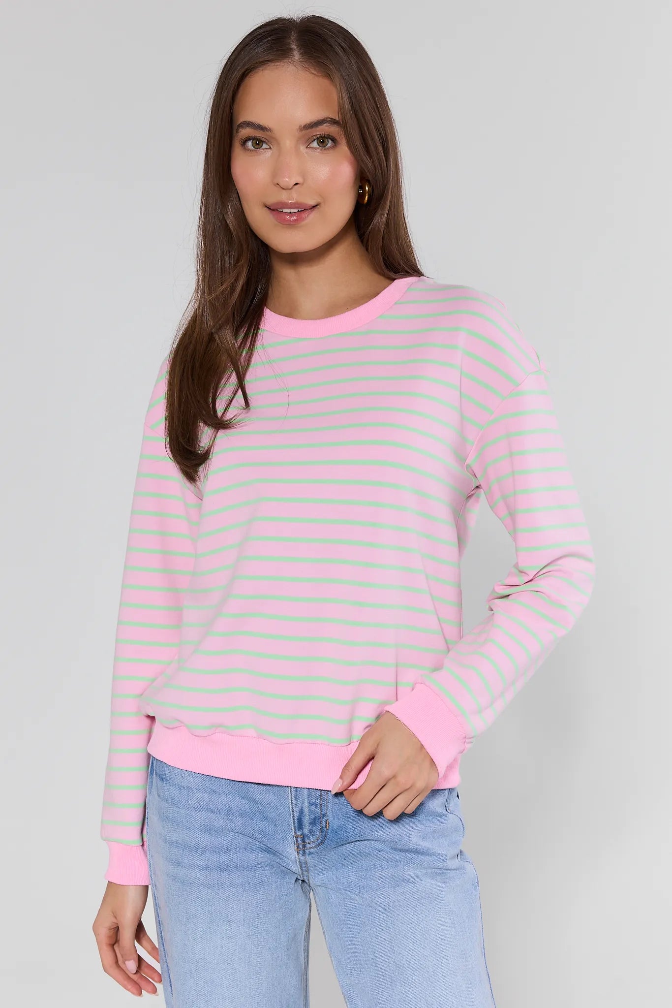 Woman wearing a pink and gray striped sweater with blue jeans on a plain background