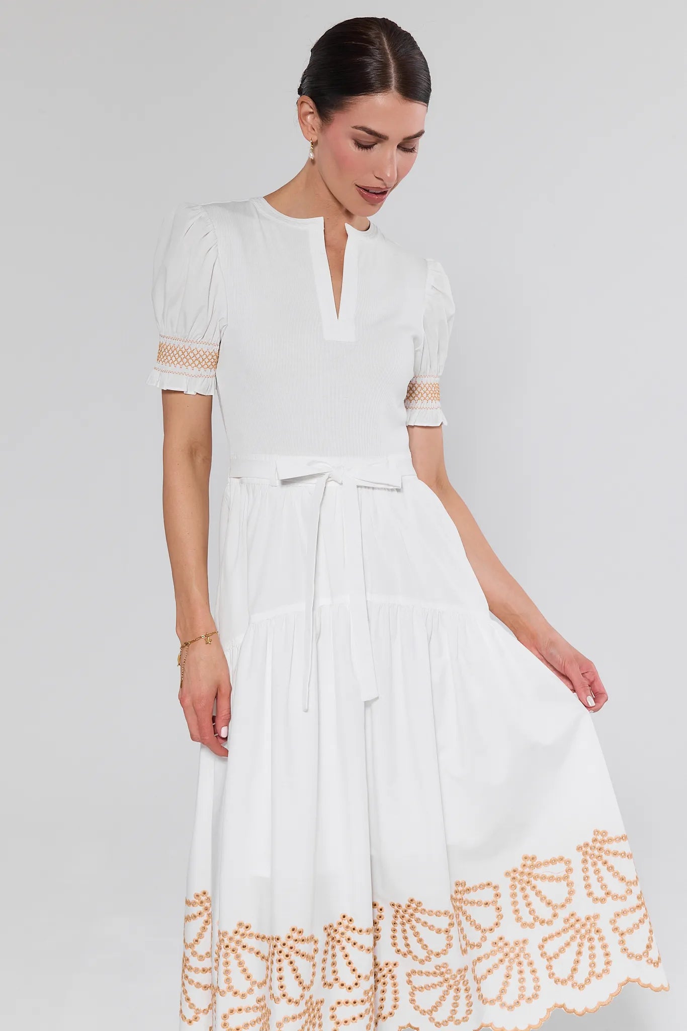 Woman wearing a white dress with lace details on a plain background