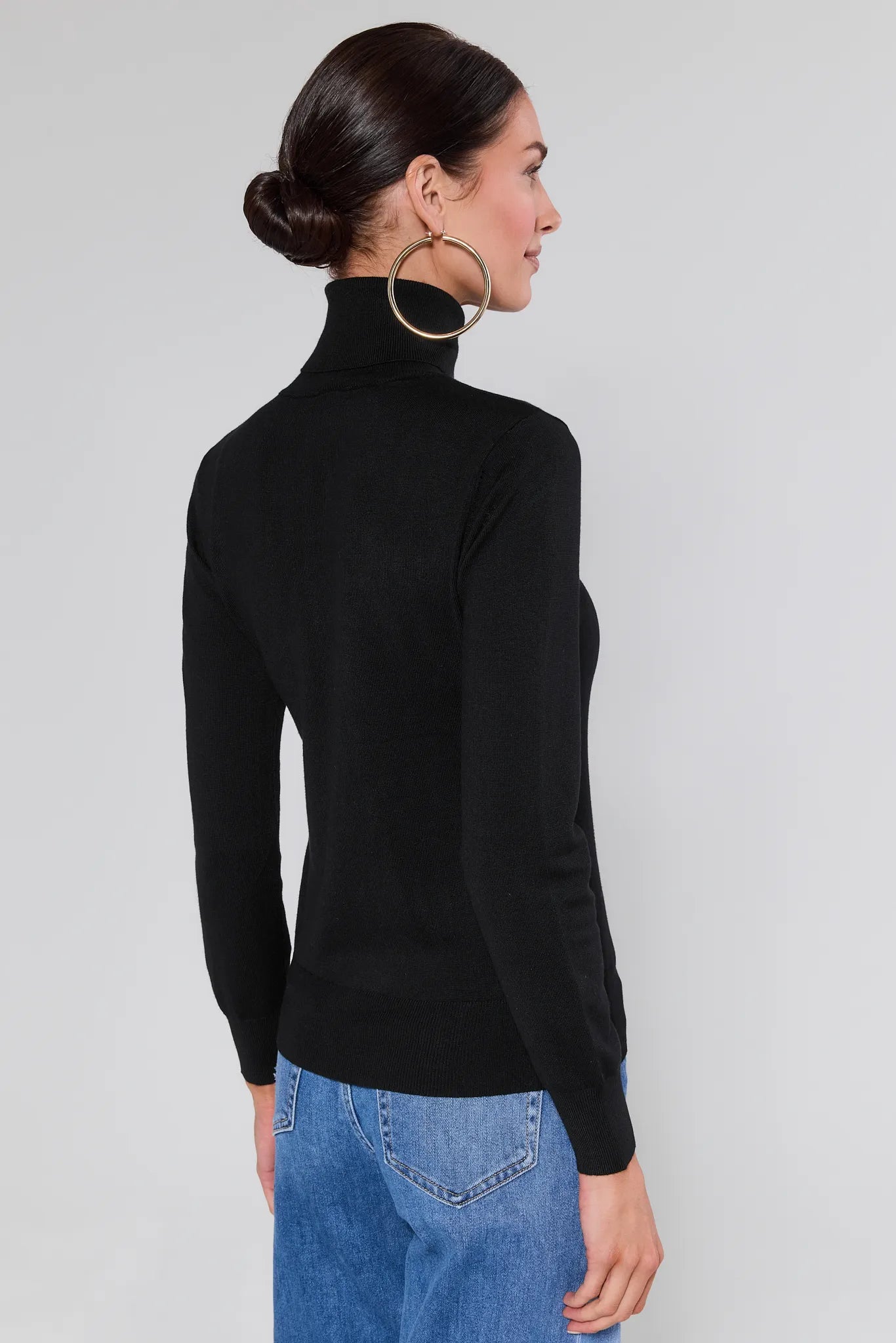 Woman wearing a Andrea Black Turtleneck Top and blue jeans against a plain background