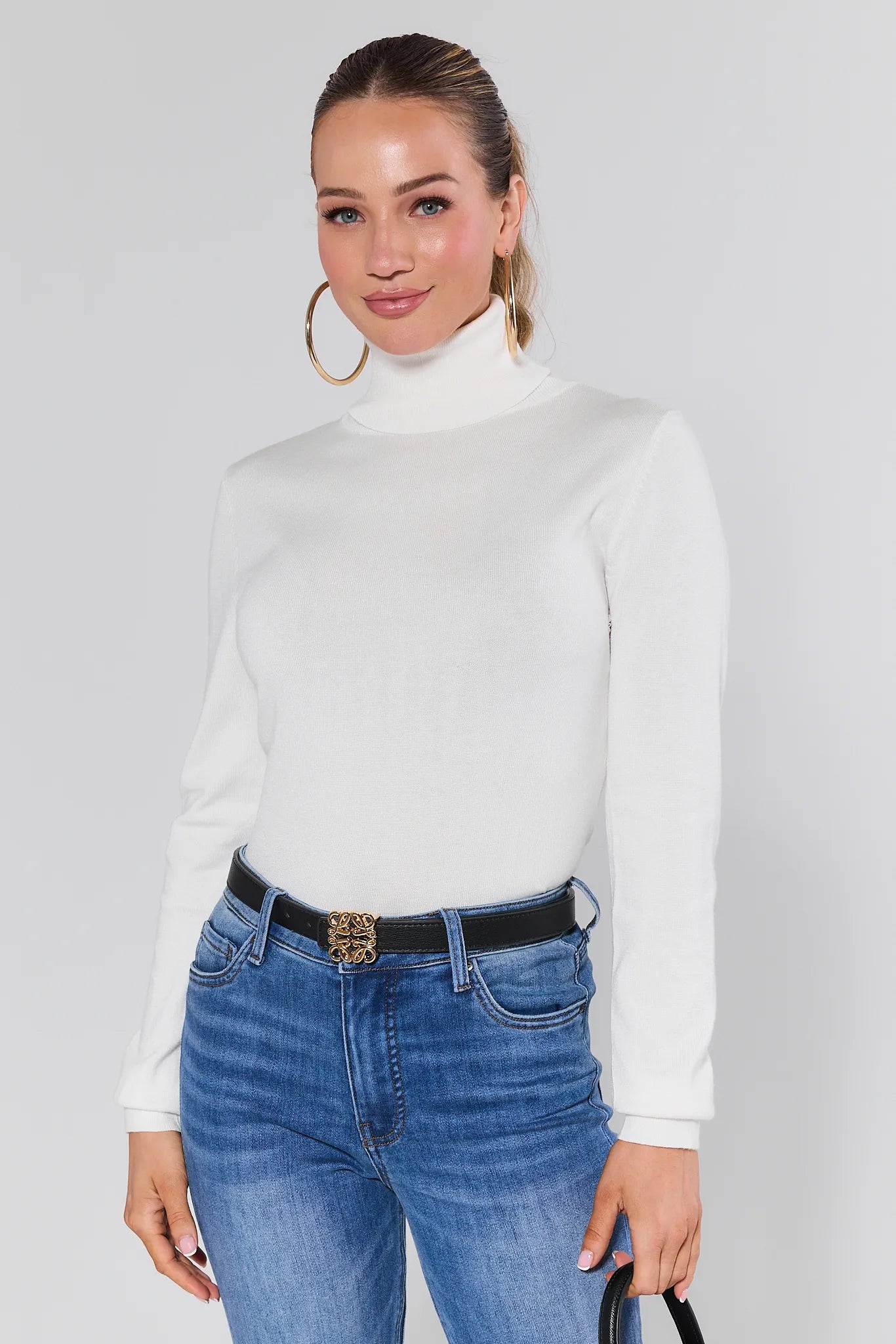 Woman wearing a Andrea Ivory Turtleneck Top and blue jeans against a plain background