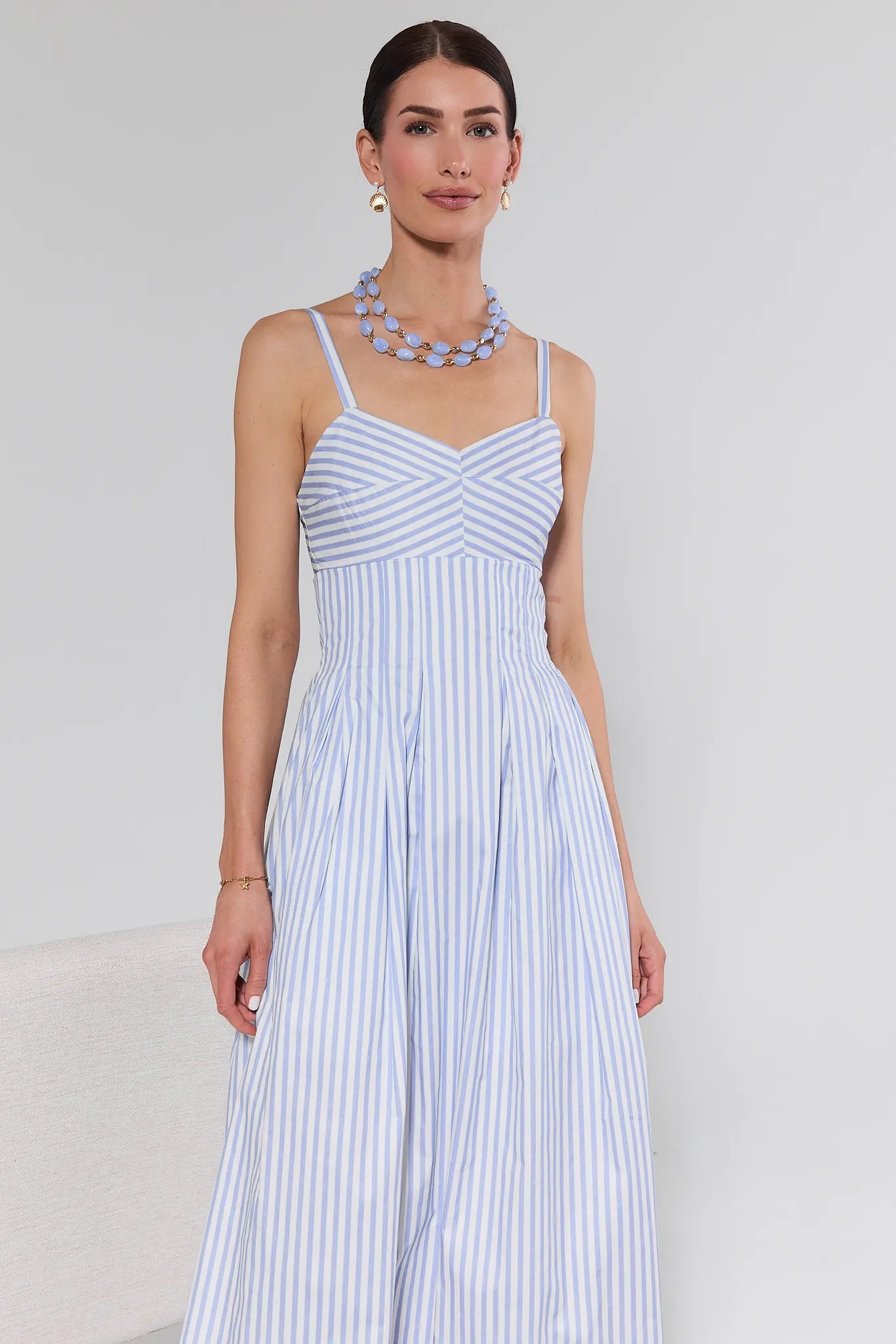 Woman wearing a blue and white striped dress with a necklace against a plain background