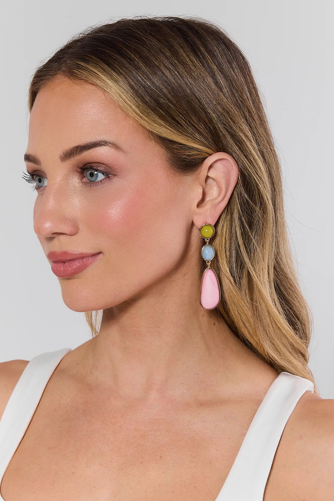 Woman wearing colorful teardrop earrings against a plain background