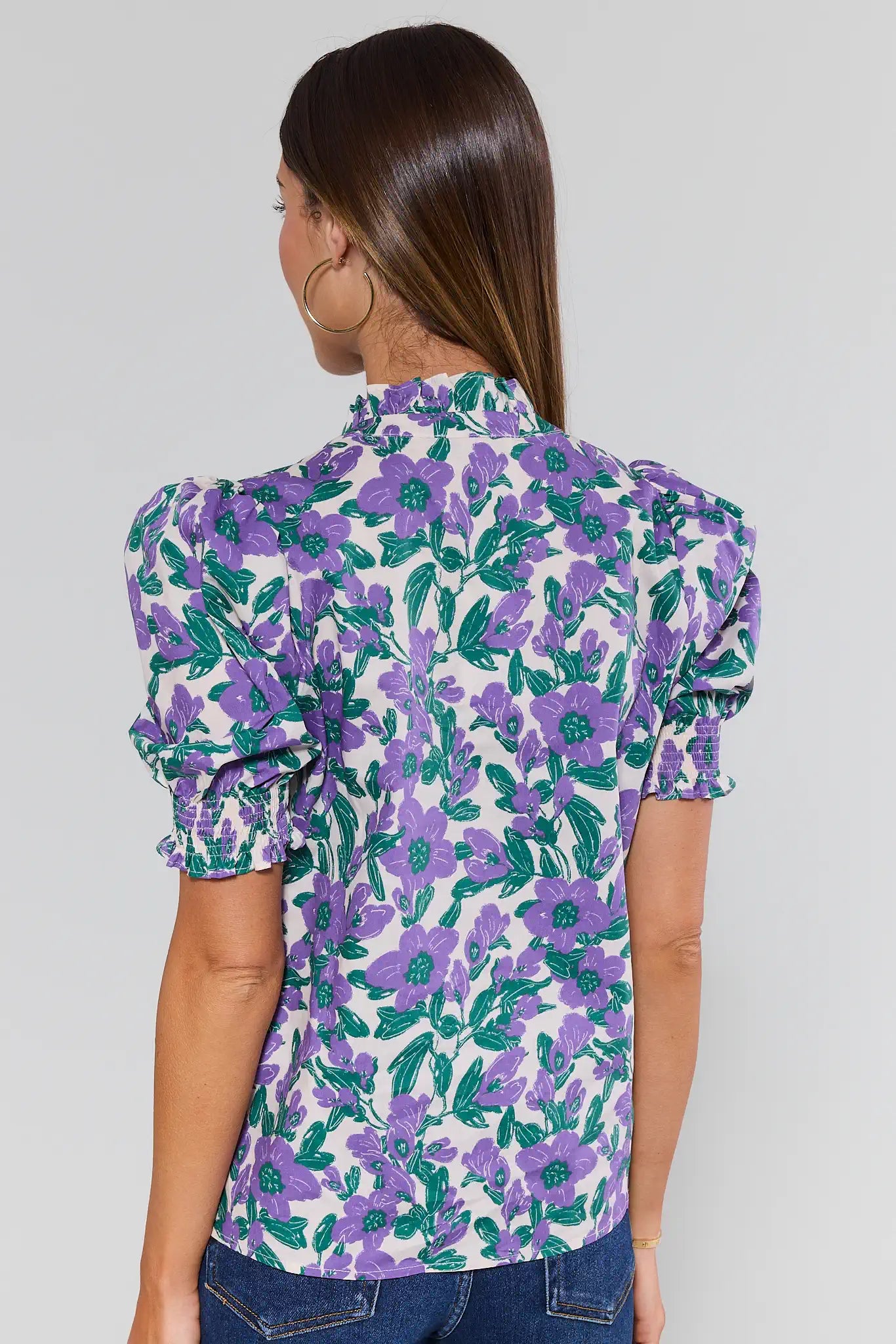 Woman wearing a floral blouse with purple and green flowers on a plain background