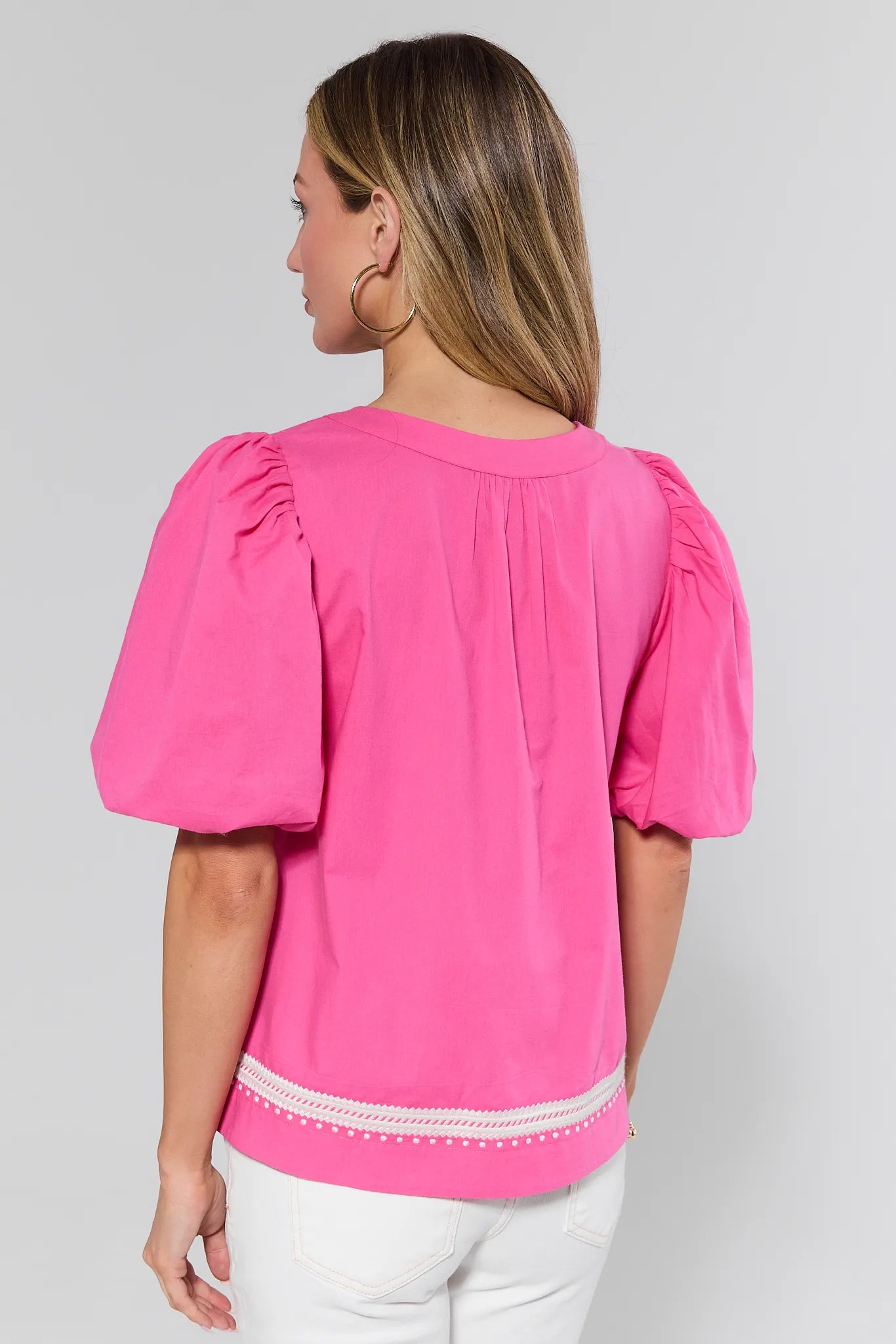 Woman wearing a pink blouse with puff sleeves on a plain background