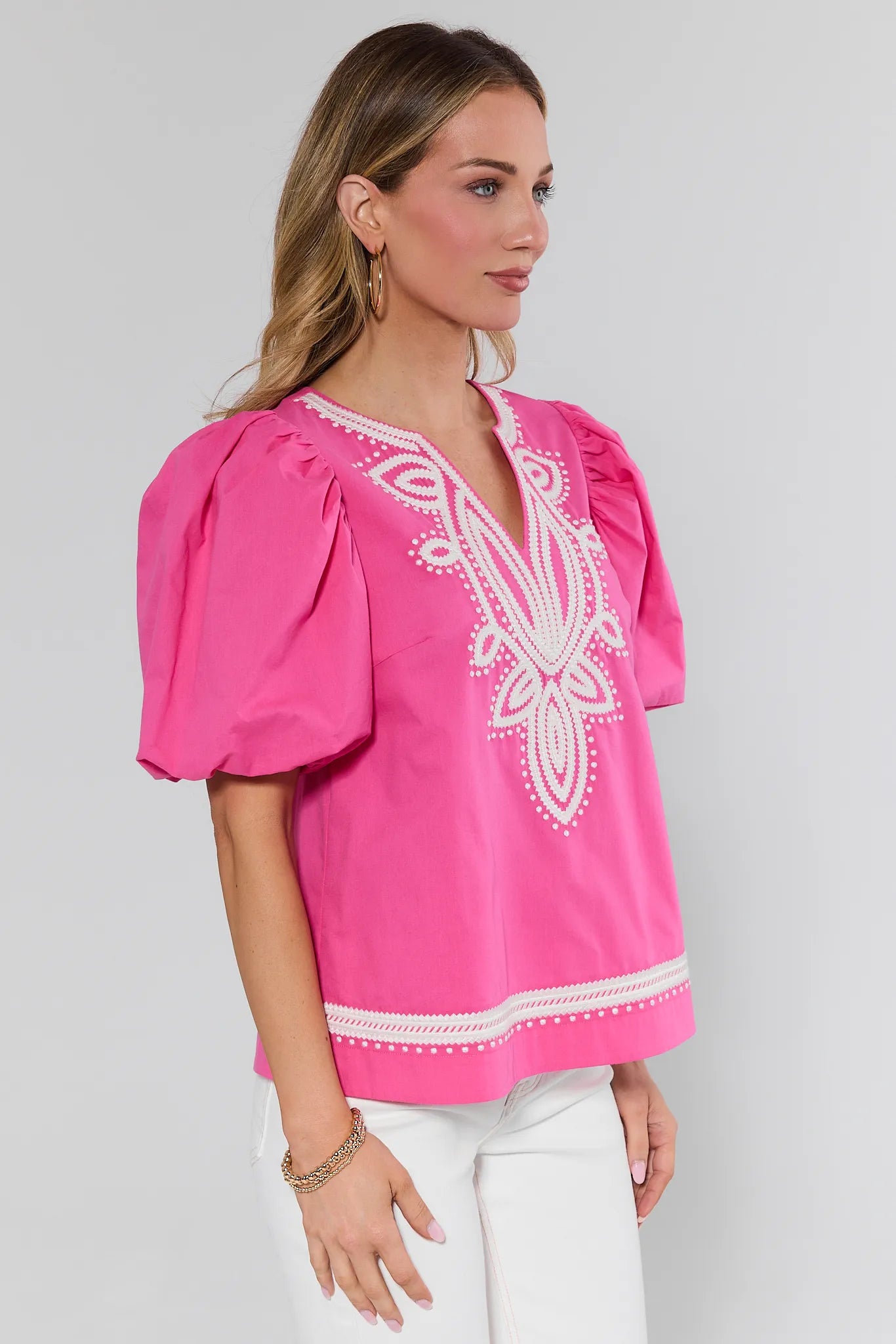 Woman wearing a pink blouse with white embroidery on a gray background