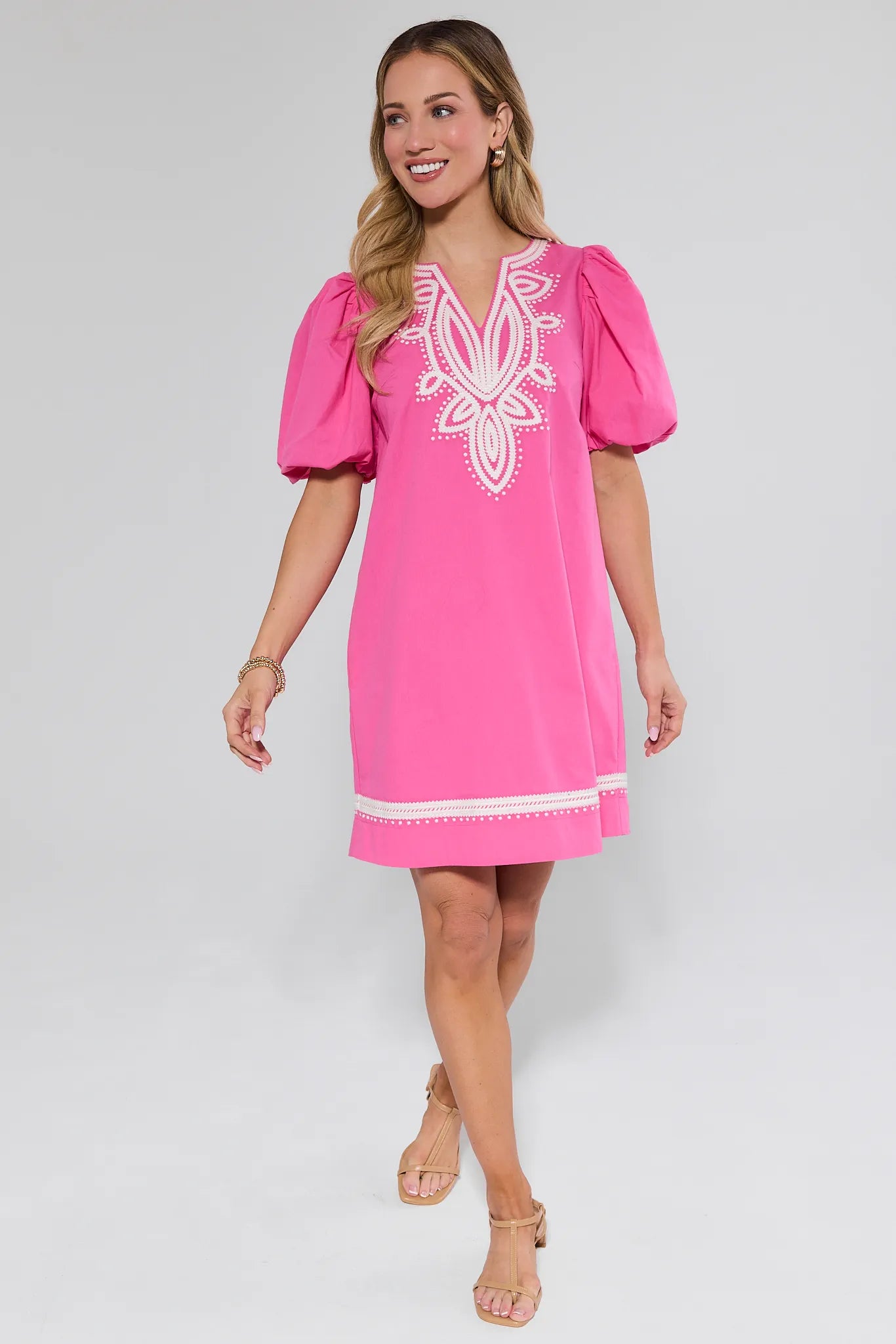 Woman wearing a pink dress with white embroidery on a plain background