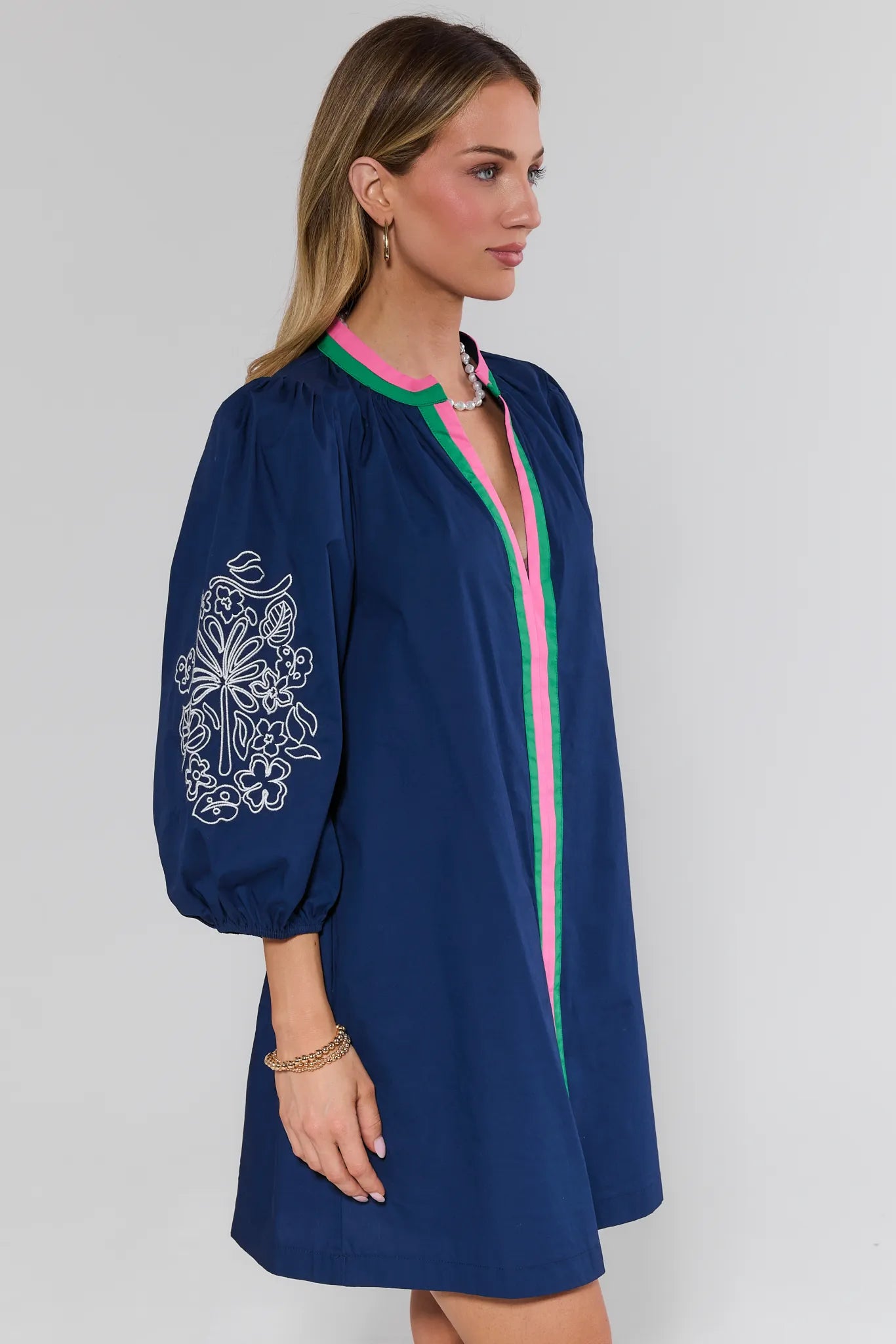 Woman wearing a navy dress with floral embroidery and pink accents on a white background