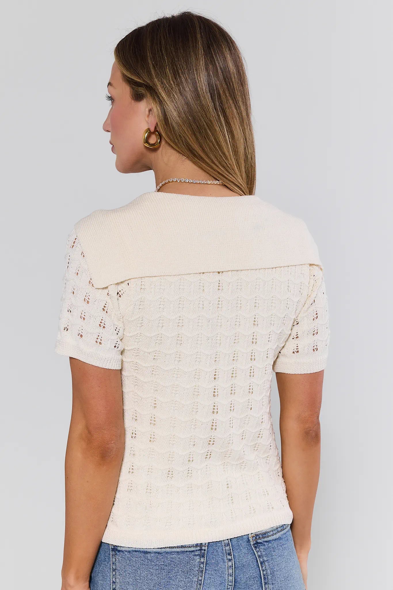 Woman wearing a cream-colored short-sleeve top with intricate detailing on a plain background