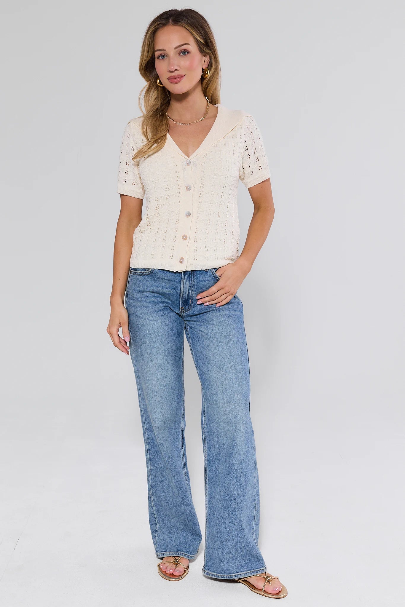 Woman wearing a white lace top and blue jeans on a plain background