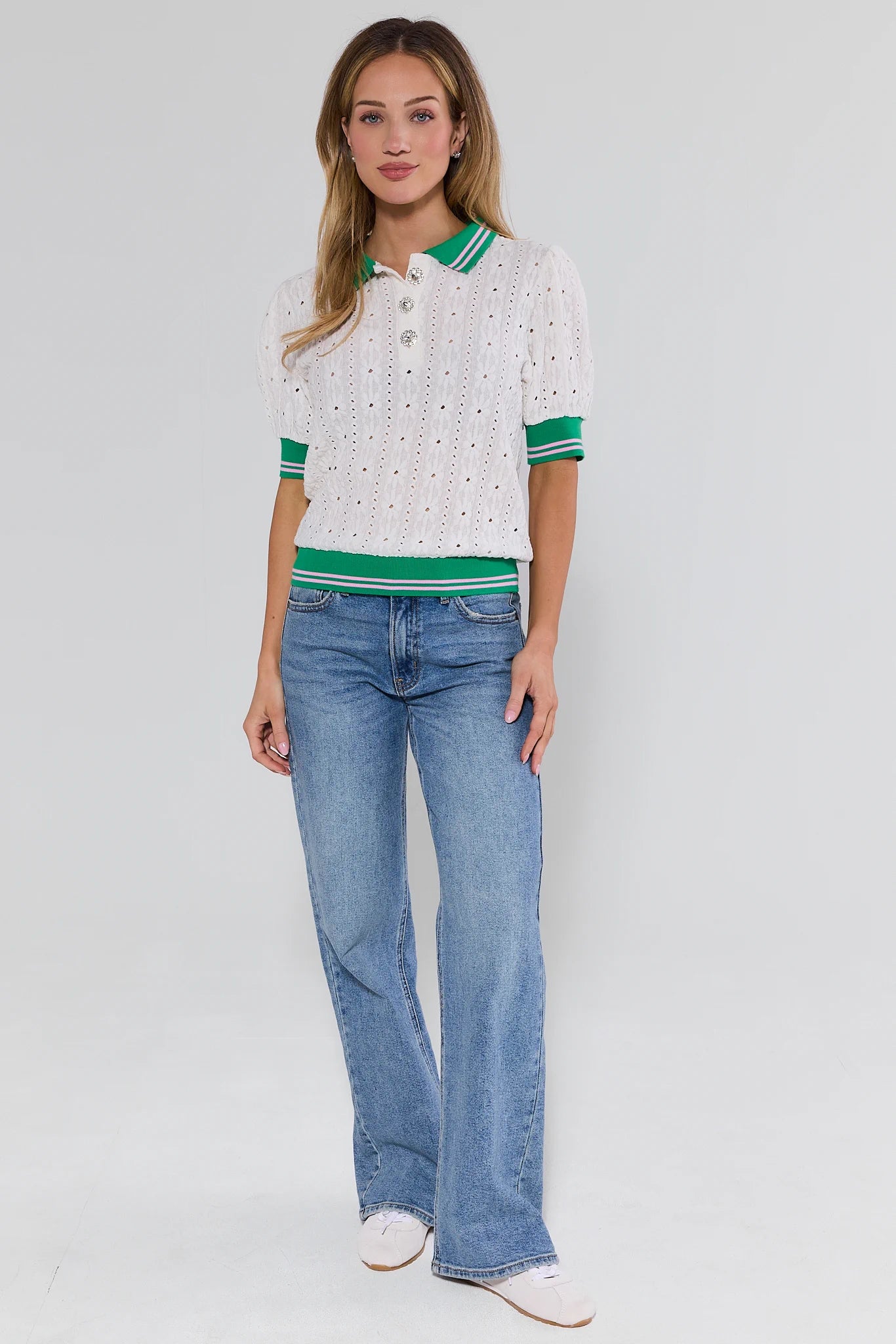Woman wearing a white polo shirt with green accents and blue jeans on a white background