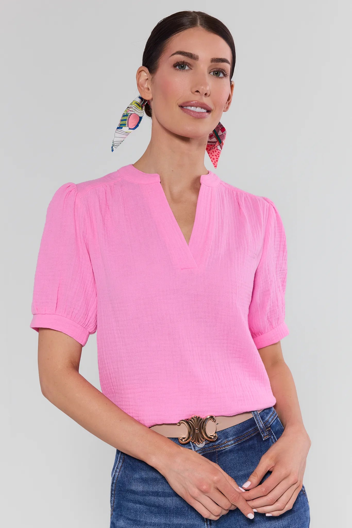 View 1: Woman wearing a pink blouse and blue jeans with a plain background