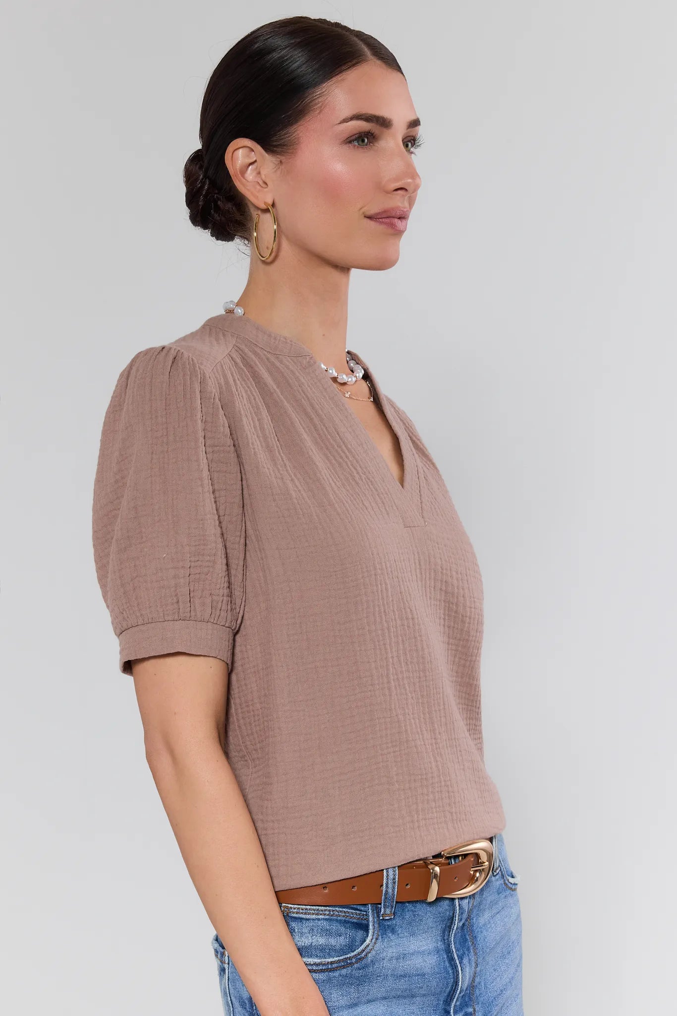 Woman wearing a brown textured top and blue jeans on a plain background