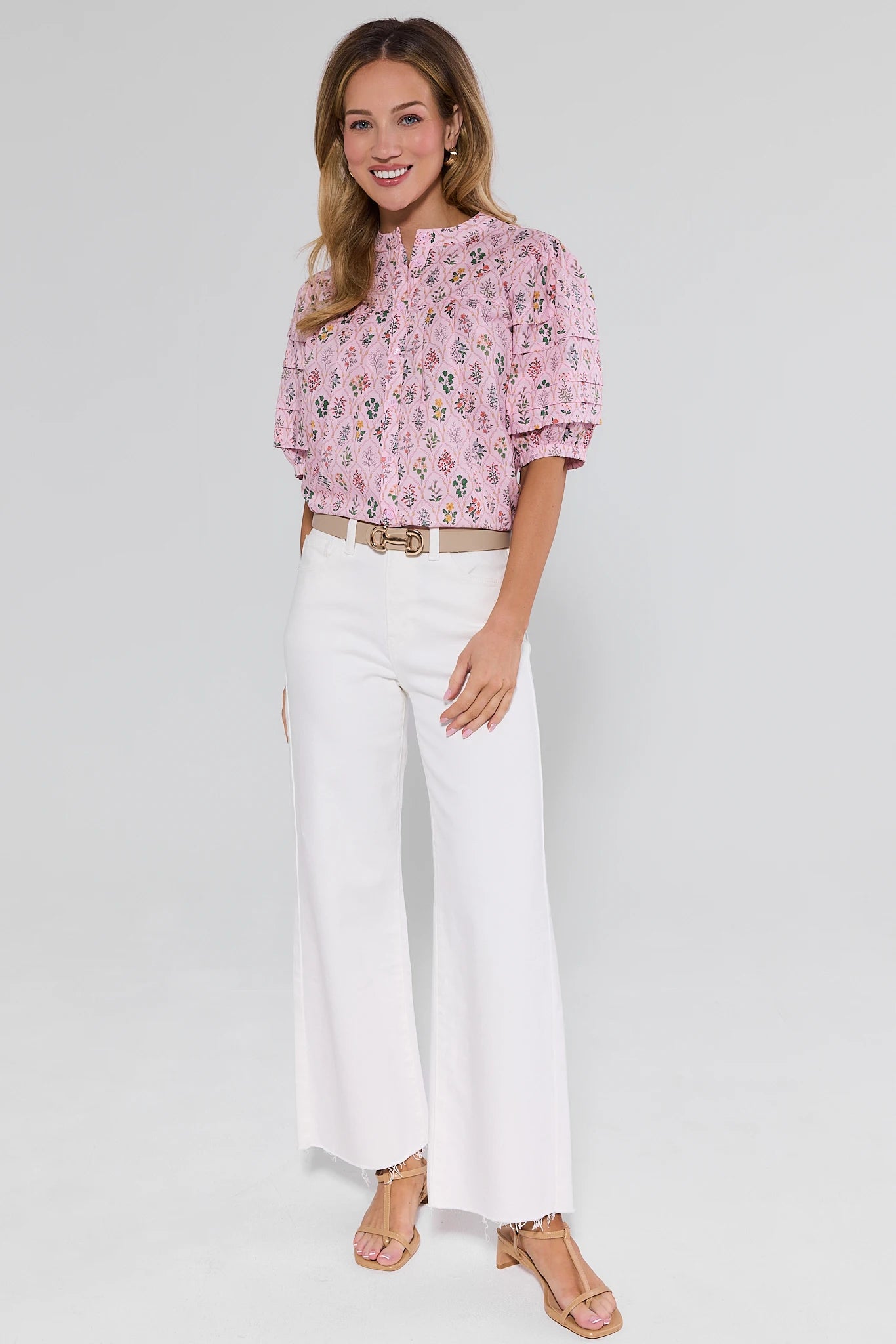 Woman wearing a pink floral blouse and white pants on a plain background