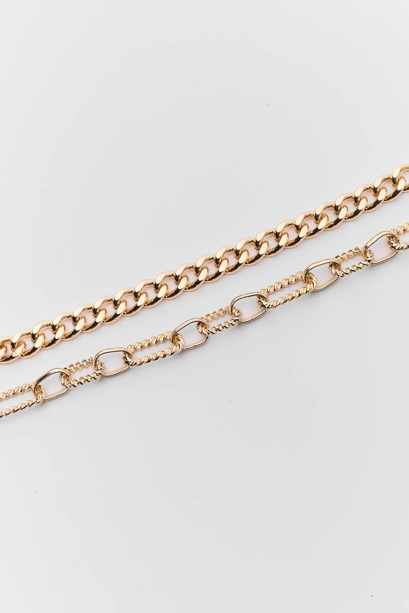 Two gold chain necklaces on a light gray background